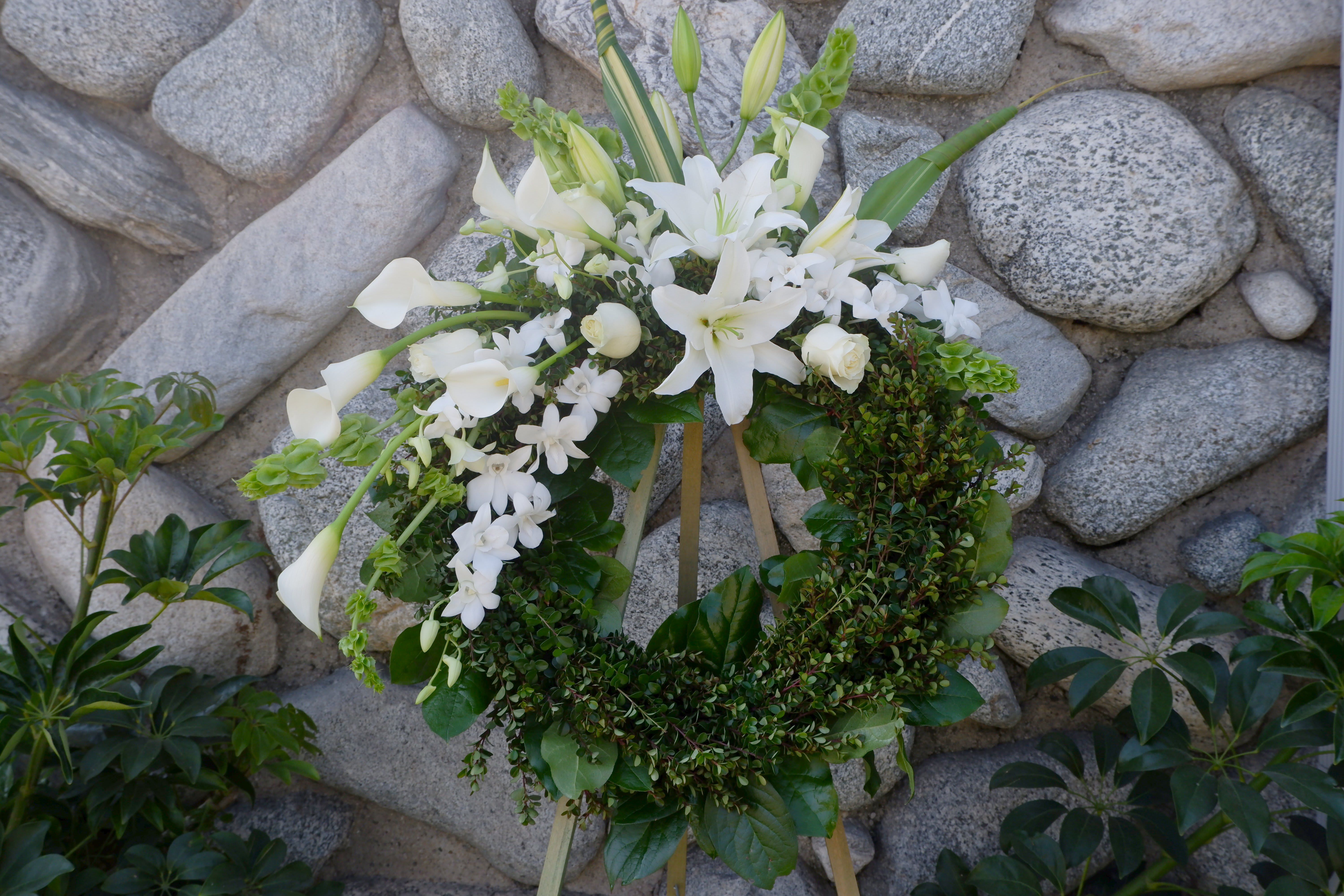 White floral wreath on a stand with lilies, calla lilies, and orchids