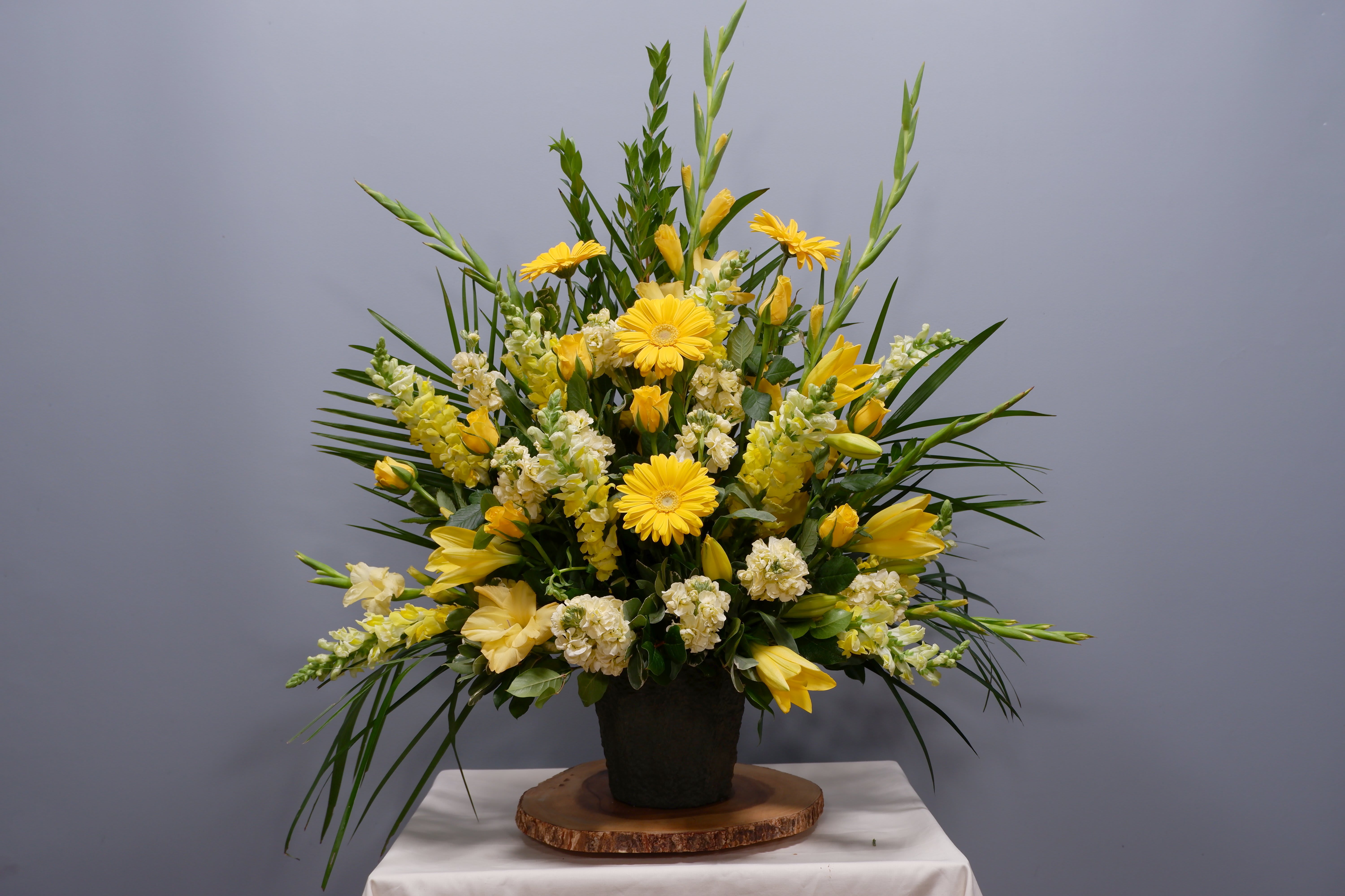 Yellow floral arrangement in a black pot with tall greenery