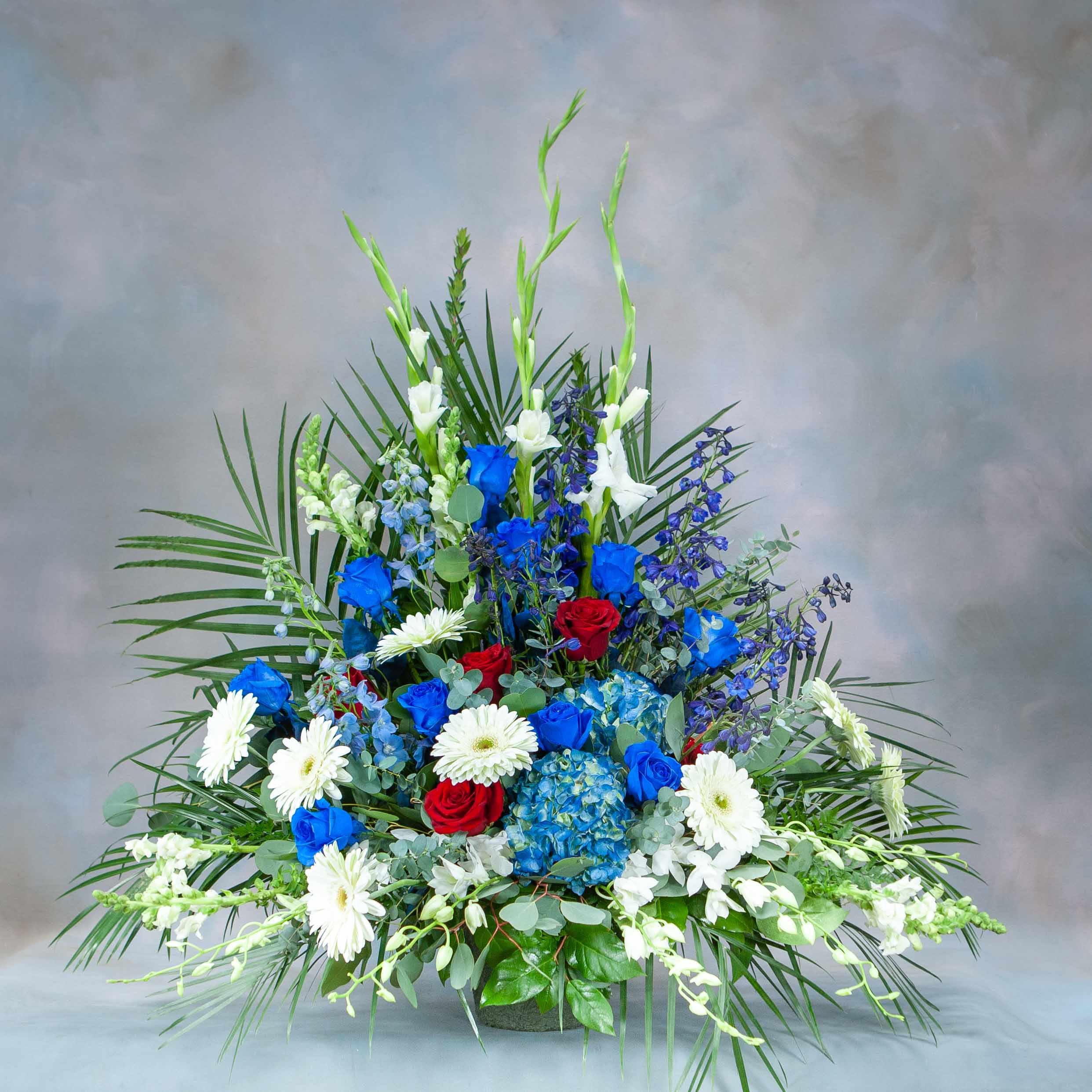 Large floral arrangement with blue, red, and white flowers in a low container