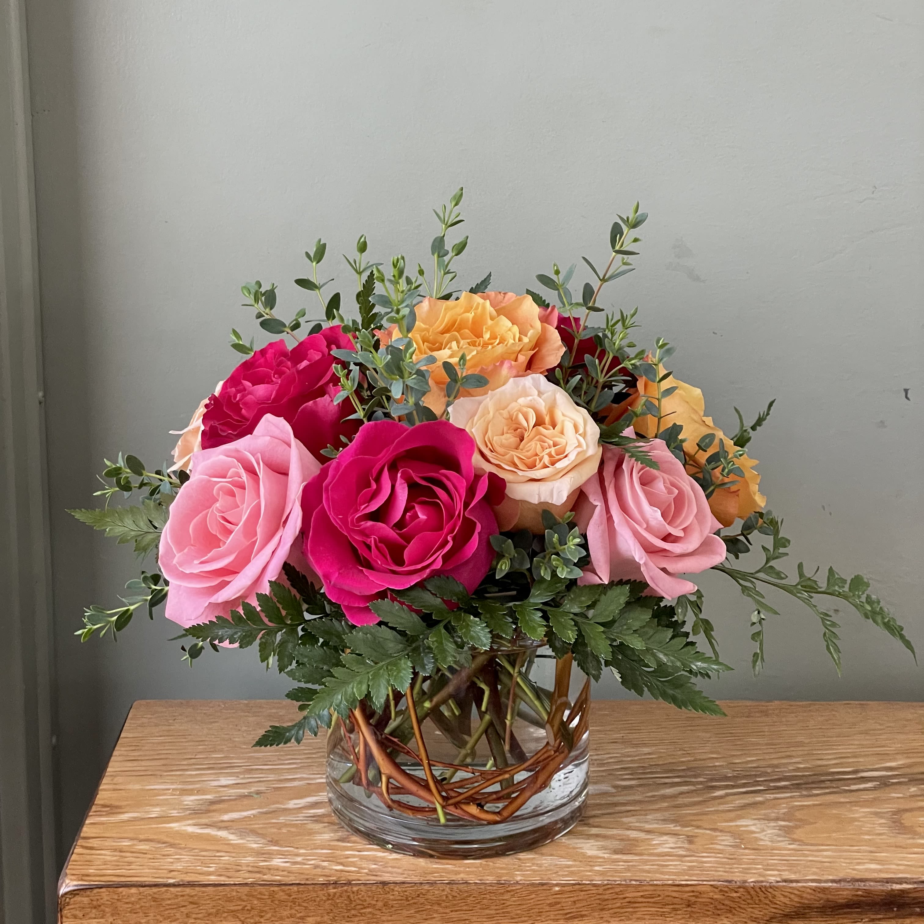 Ring Around the Rose-y (SF120) - A bright, rounded cluster of mixed roses makes a joyful centerpiece that says "thinking of you" without words-perfect as an anniversary bouquet, birthday surprise, or Mother's Day gift. This flower arrangement brings together warm seasonal tones in a low, clear glass vase, creating a look that's equally right for love and romance, a housewarming, or simply a spontaneous "just because" moment.  The Ring Around the Rose-y arrangement features a dense, circular grouping of fresh roses arranged in a full, rounded dome. Airy greenery lifts and frames the blooms, giving a fresh garden feel and subtle texture against the smooth petals. The design is compact yet lush, ideal for tabletops and smaller spaces.  Give this to the friend, partner, or family member you want to make feel seen; she'll feel genuinely celebrated whether it's for Valentine's Day, Women's Day, Best Friends Day, a thank-you, or just because. The arrangement arrives ready to display and benefits from regular water changes and a cool spot away from direct heat to keep the roses looking their best.