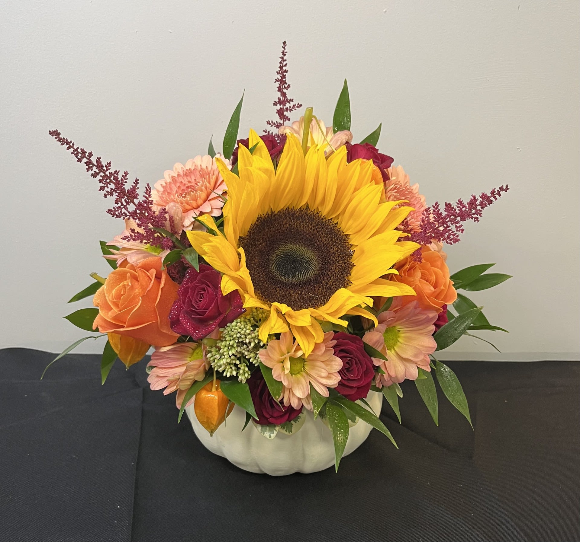 Pumpkin Pixie Garden by Chasing Petals - Add a touch of magic to your fall decor with our Pumpkin Pixie Garden! This enchanting arrangement features a joyful mix of golden sunflowers, peachy-pink mums, vibrant roses and airy sprigs of astilbe - all nestled in a charming ceramic pumpkin. Perfect for brightening any table, gifting to a loved one, or simply celebrating the beauty of autumn with a little floral whimsy.   Ceramic Pumpkin is available in white and orange.