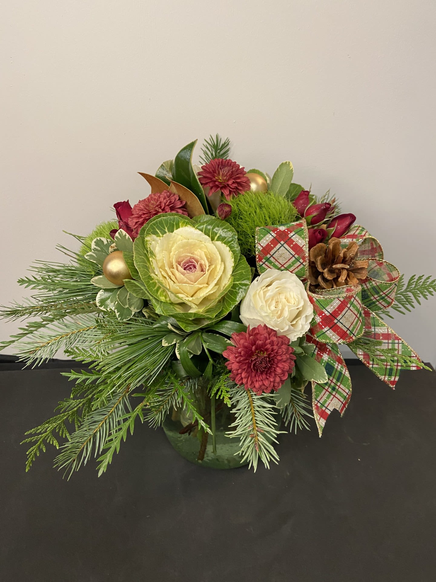 Winter Bourdeaux Bloom by Chasing Petals - Winter Boudreaux Bloom showcases a refined blend of rich seasonal textures, featuring lush evergreens, elegant winter blooms, and warm touches of burgundy and gold. Designed with timeless sophistication and accented by classic tartan ribbon, this arrangement brings an elevated, estate-inspired charm to any holiday setting. Perfect for gifting or adding a luxurious touch to your own winter décor.