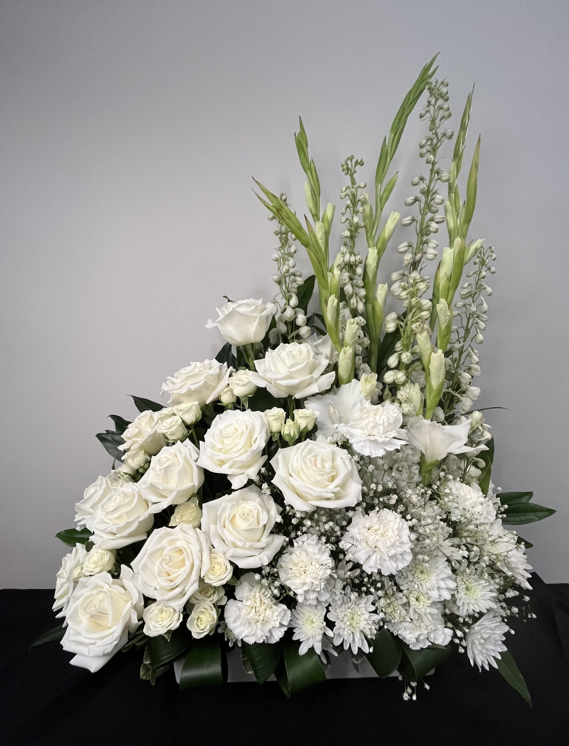 Eternal Light by Chasing Petals - Eternal Light is a graceful all-white arrangement that symbolizes peace, remembrance, and enduring love. Featuring elegant roses, delicate spray blooms and soft accent flowers riding among lush greenery, this design offers a sense of calm and quiet reflection. Its timeless beauty makes it a heartfelt tribute, honoring a life remembered and a light that continues to shine.