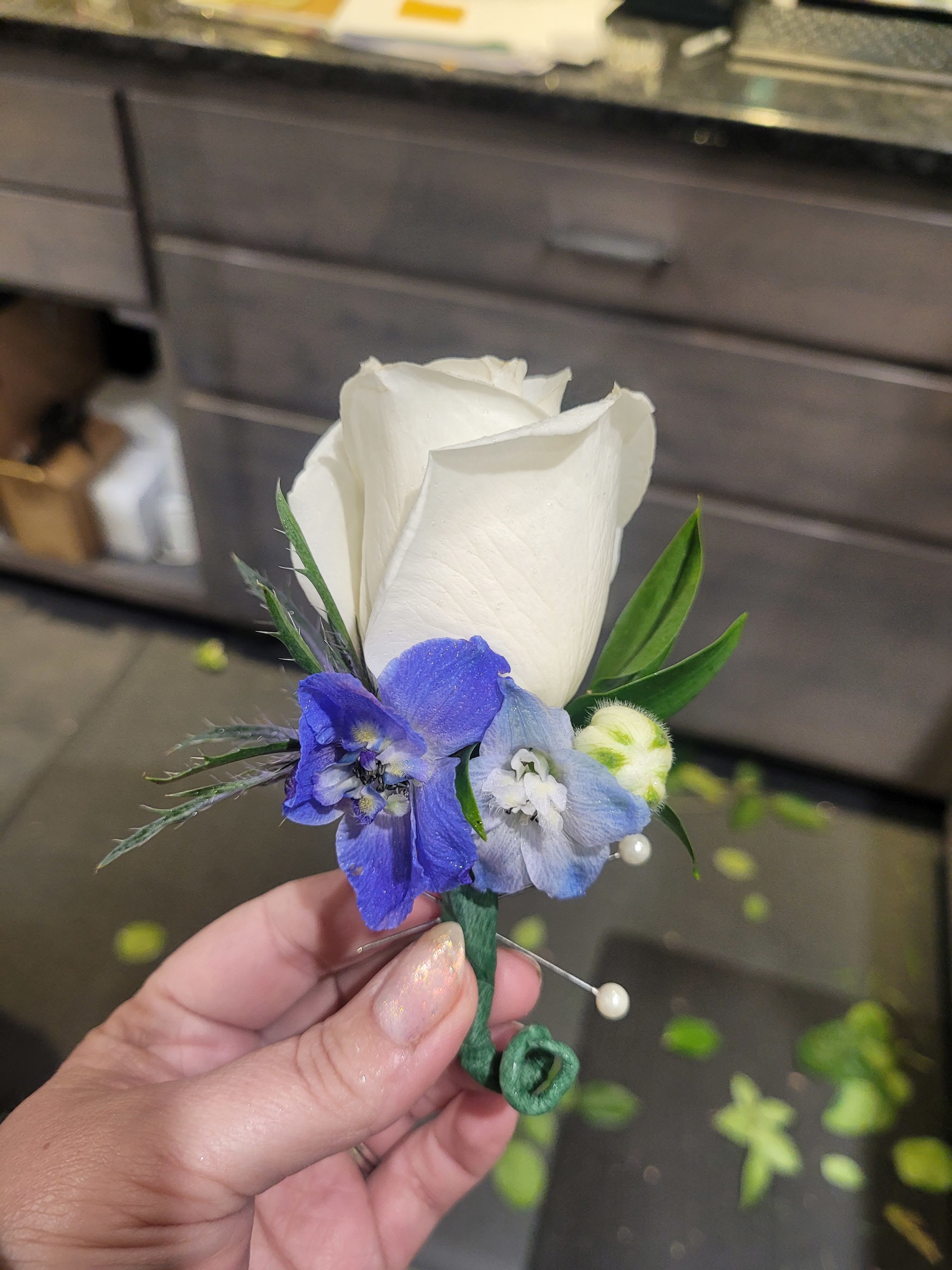 White rose boutonniere with blue flowers and green accents