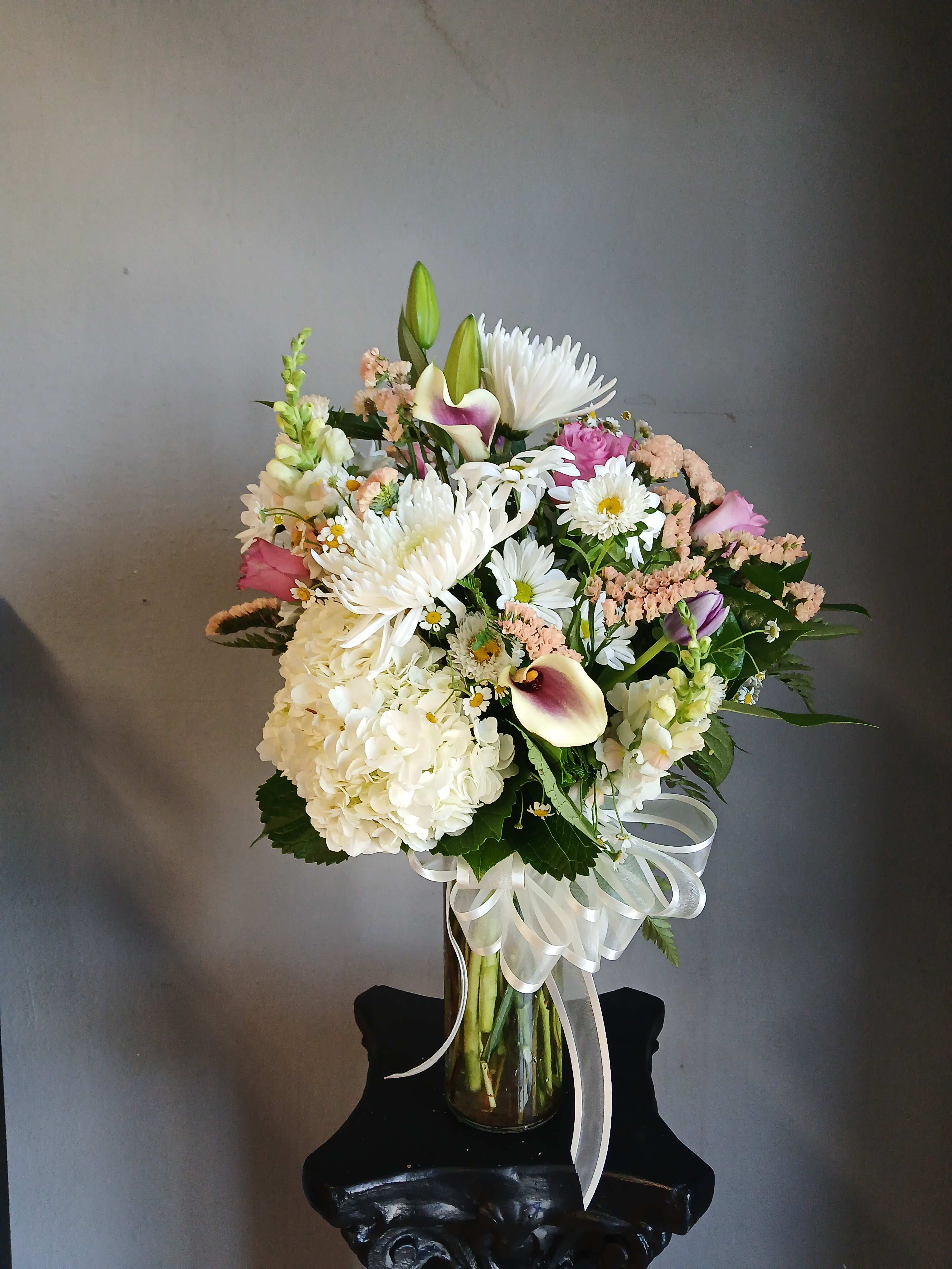 Mixed bouquet of white, pink, and purple flowers in a glass vase with a white ribbon