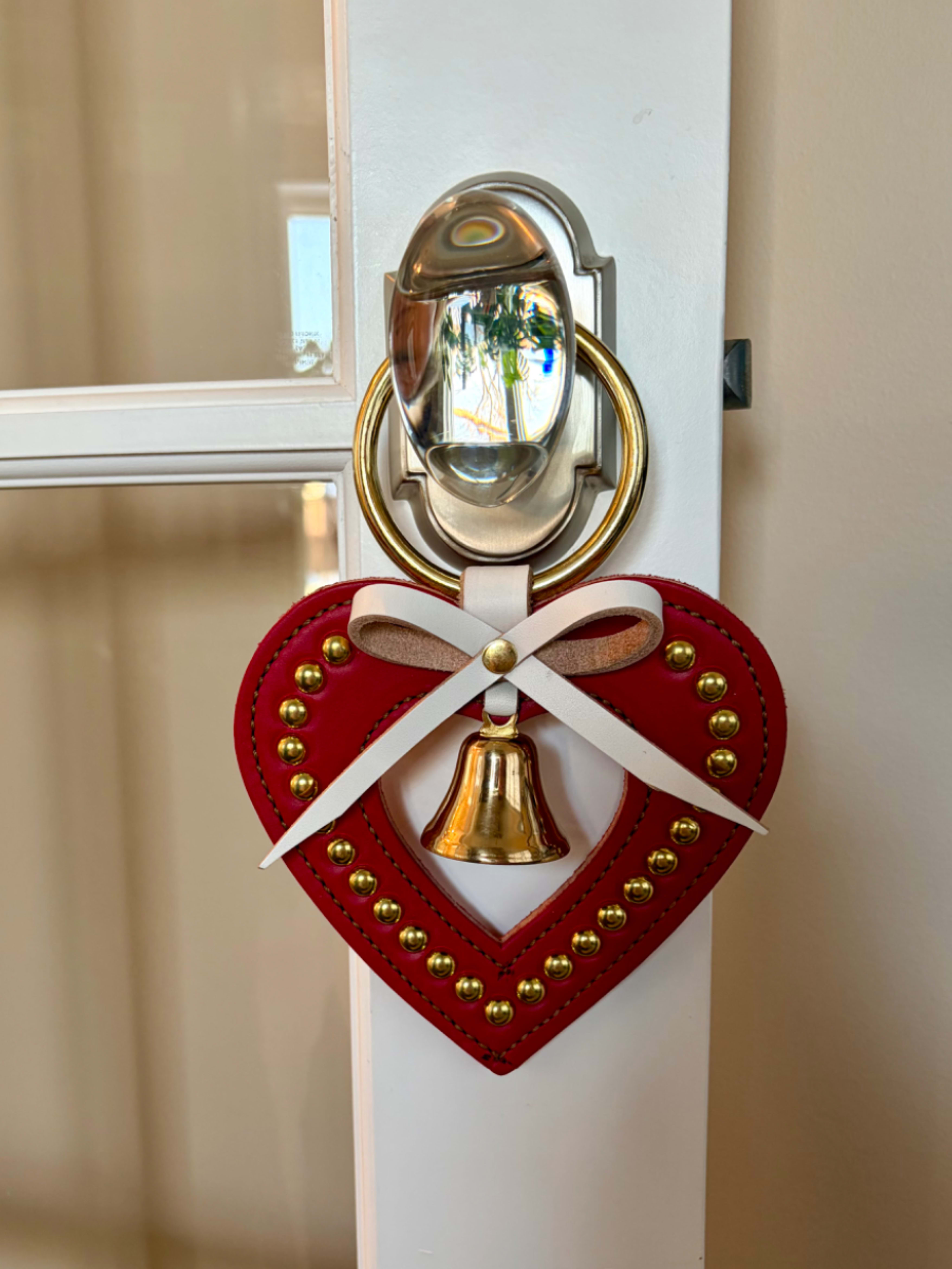Red heart-shaped door hanger with a white bow and brass bell