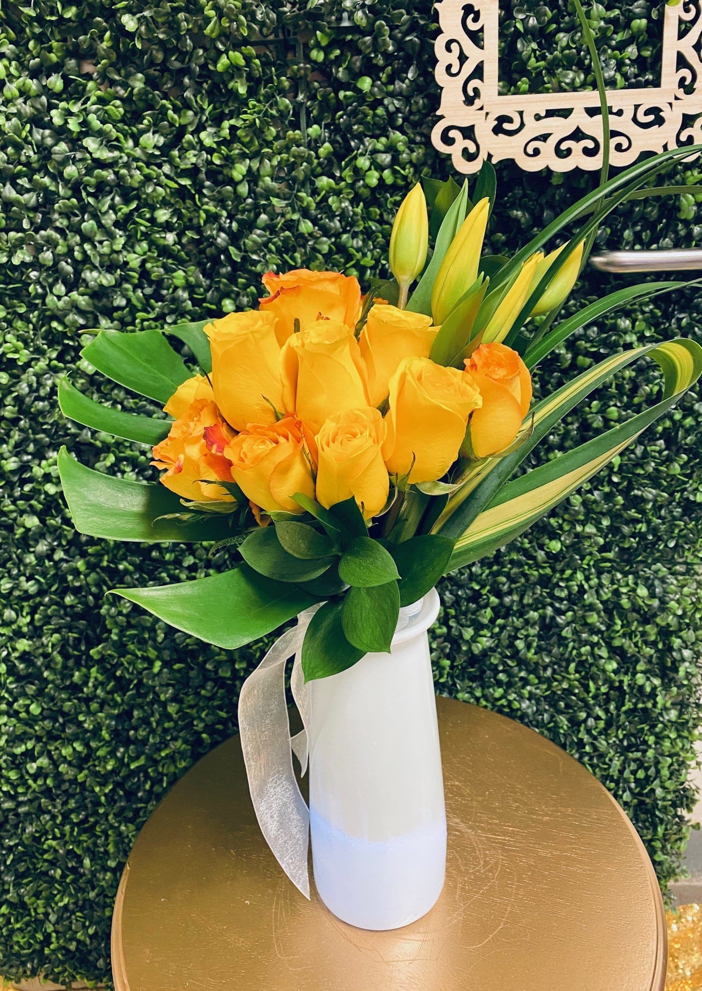 Yellow and orange roses in a white vase with a silver ribbon