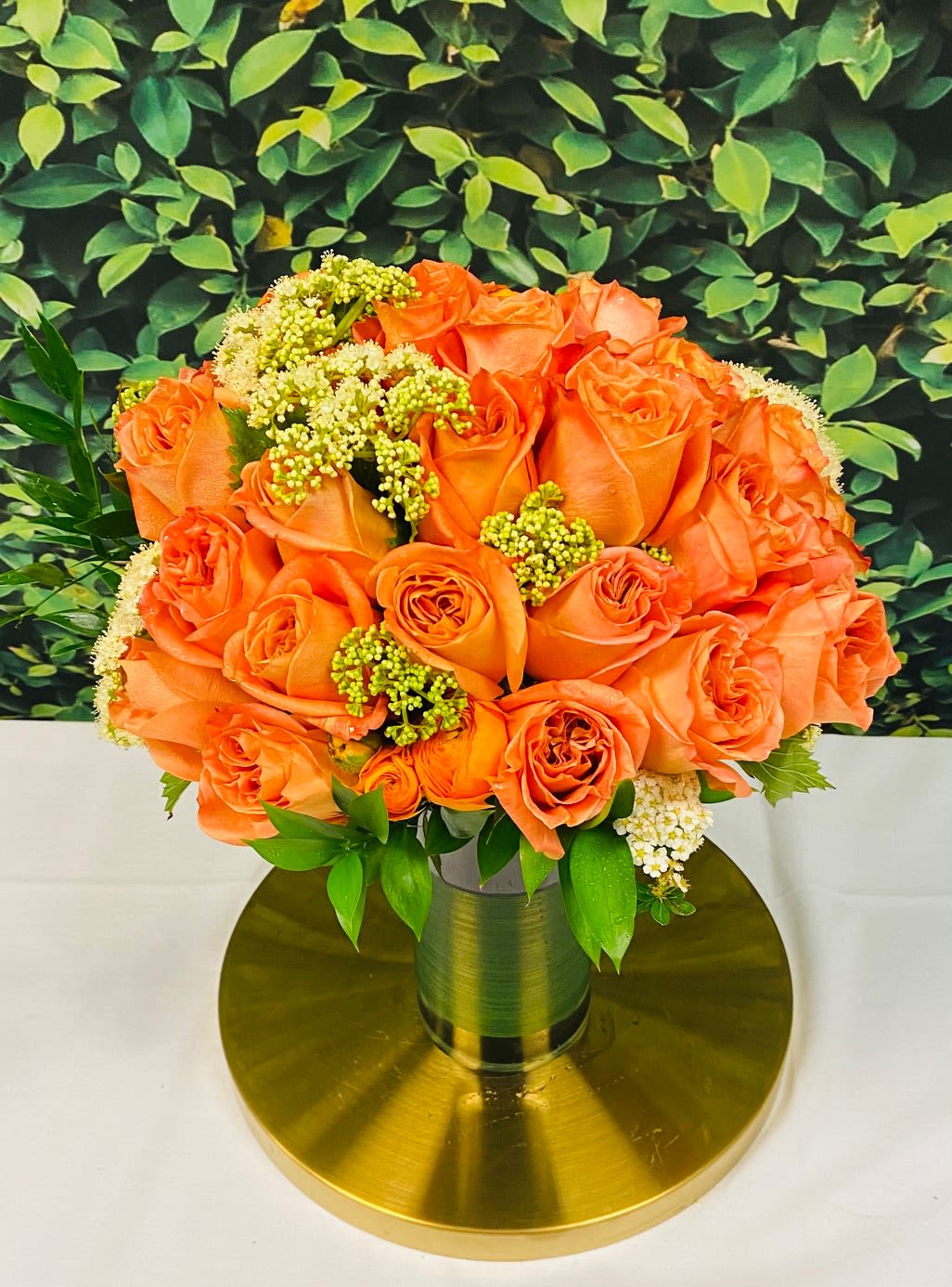 Orange roses arranged in a gold vase on a round gold base
