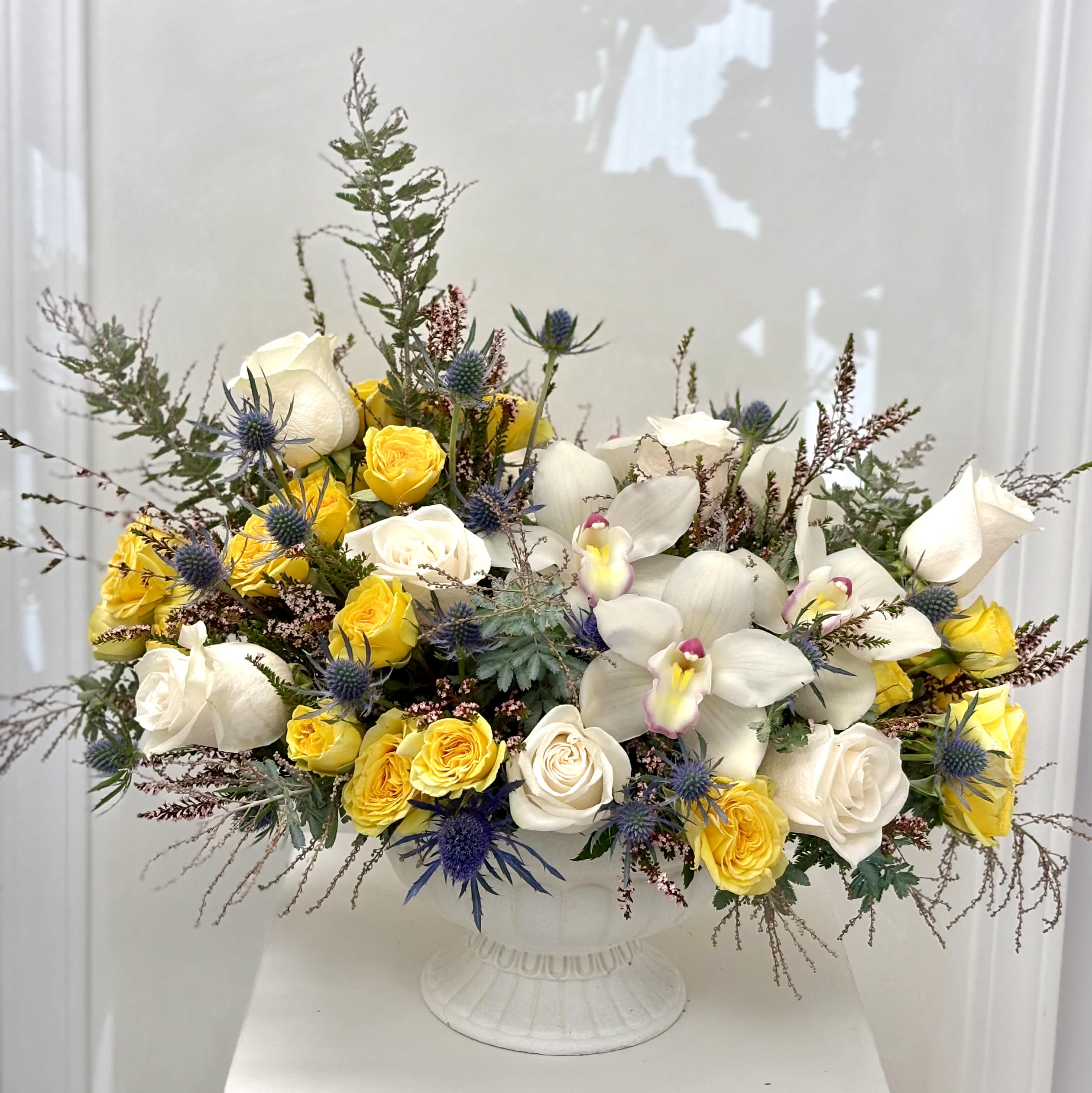 White and yellow roses with white orchids in a white pedestal vase