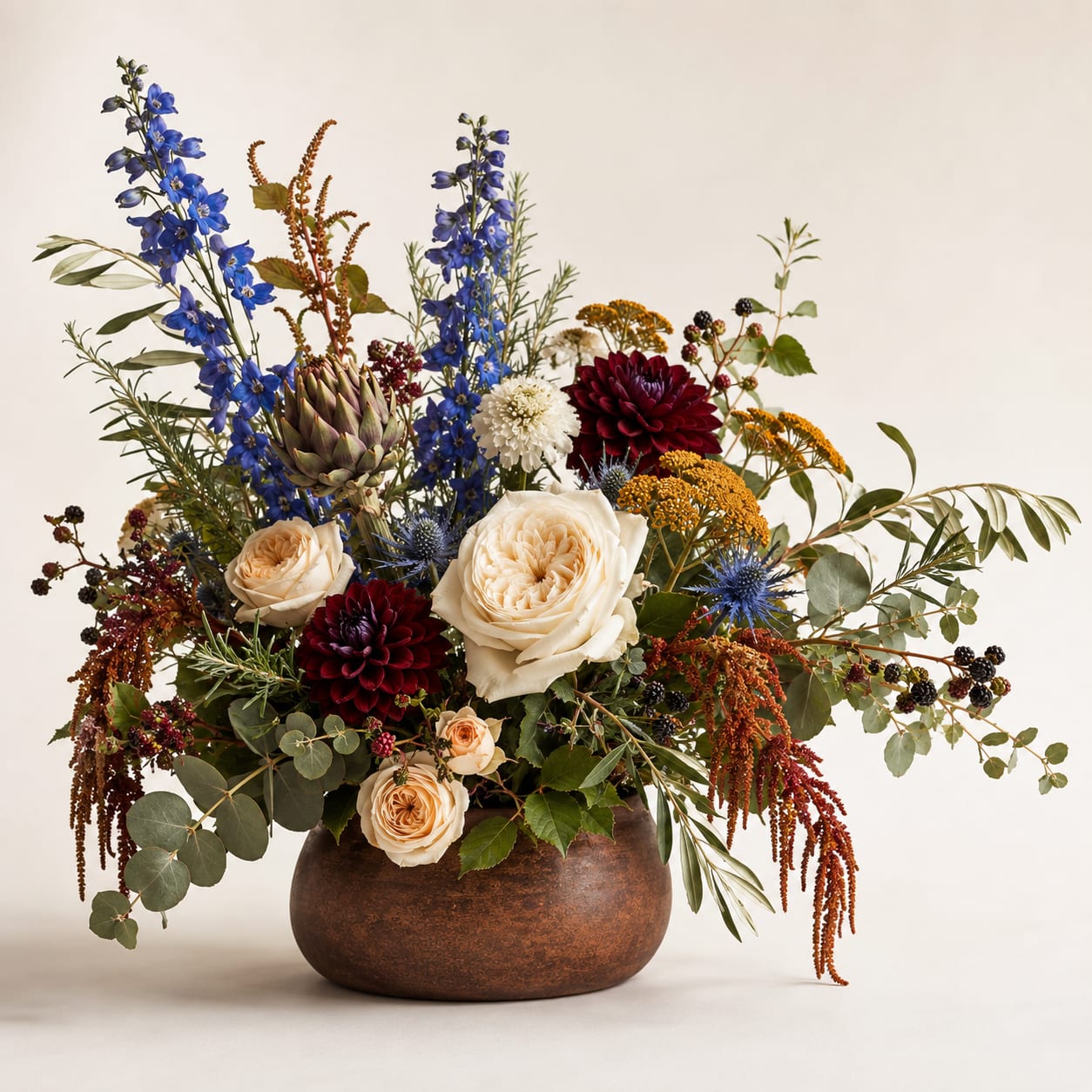 Mixed bouquet in a round brown vase with blue, cream, and burgundy flowers