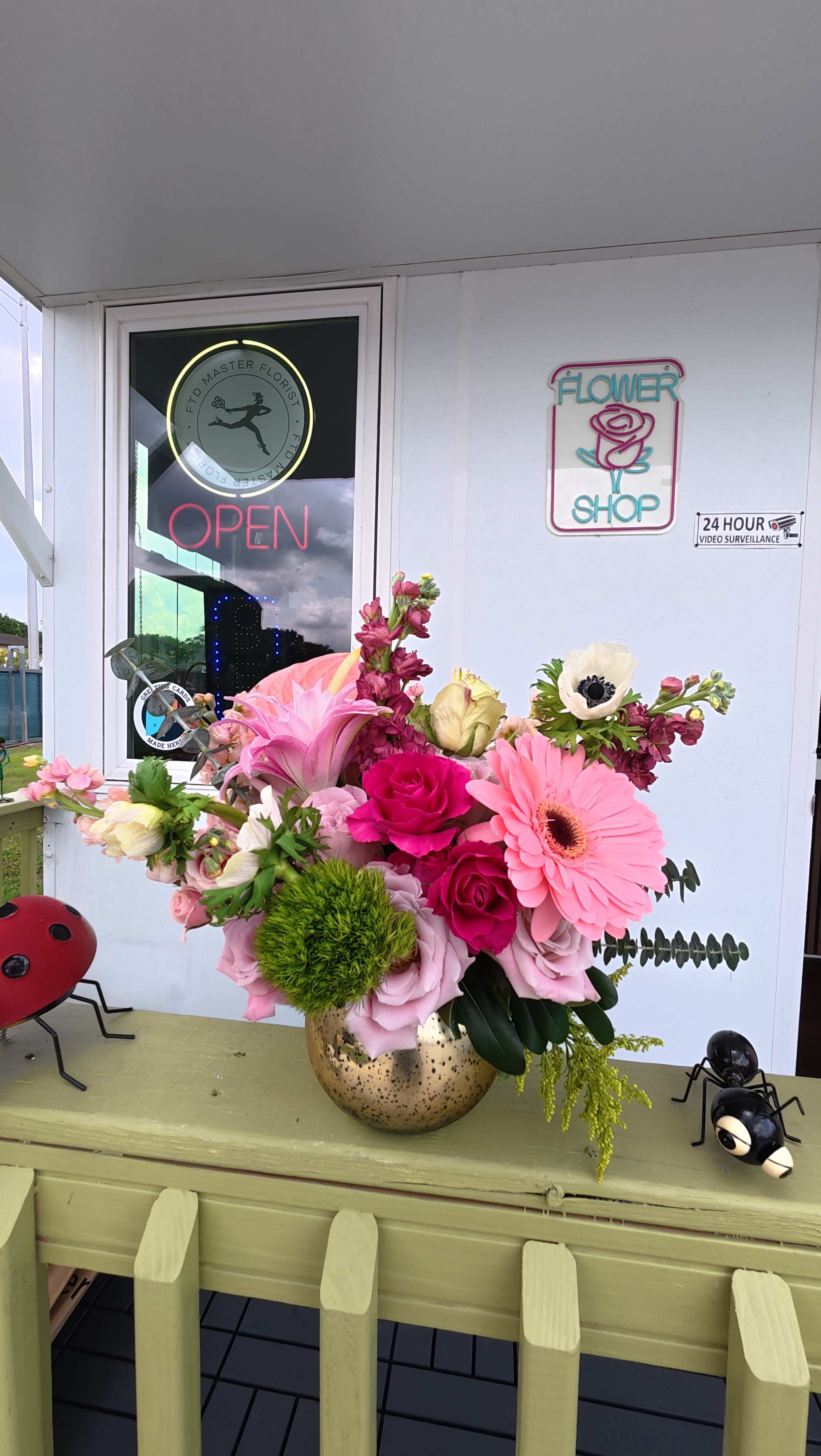 Pink and white floral arrangement in a gold vase on a porch