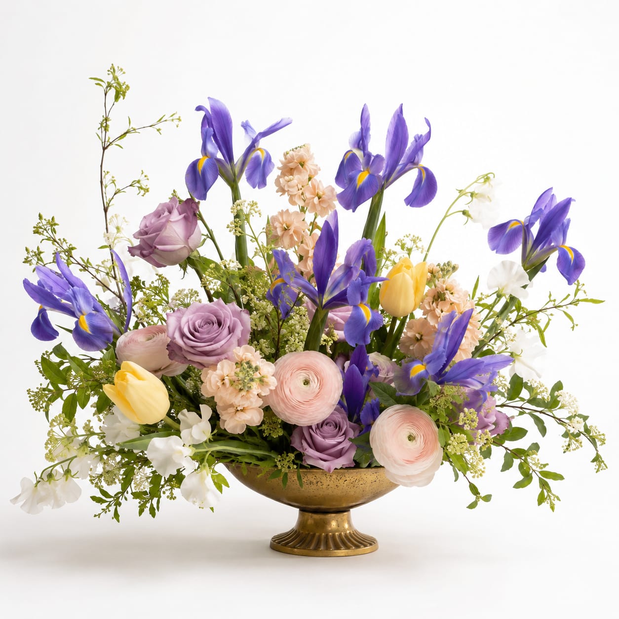 Mixed bouquet of purple irises, roses, and pastel flowers in a gold bowl vase