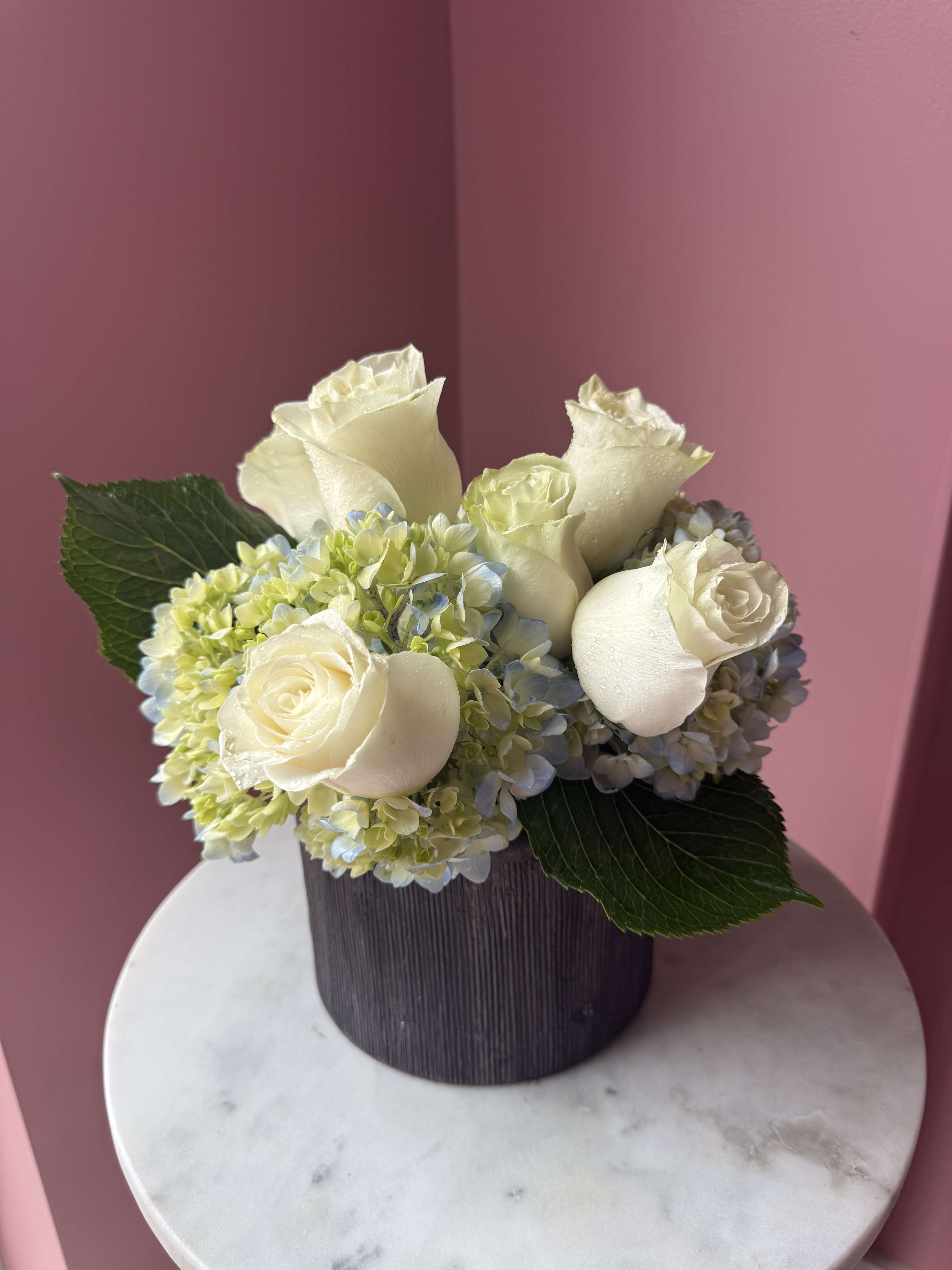 Cream roses and pale hydrangeas in a dark round vase
