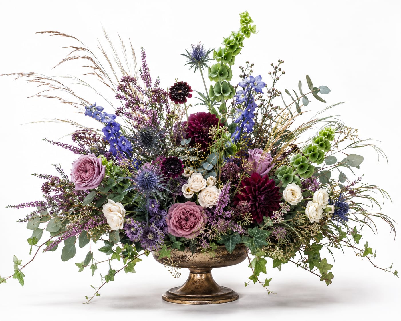 Mixed floral arrangement in a gold pedestal vase with purple, white, and green blooms