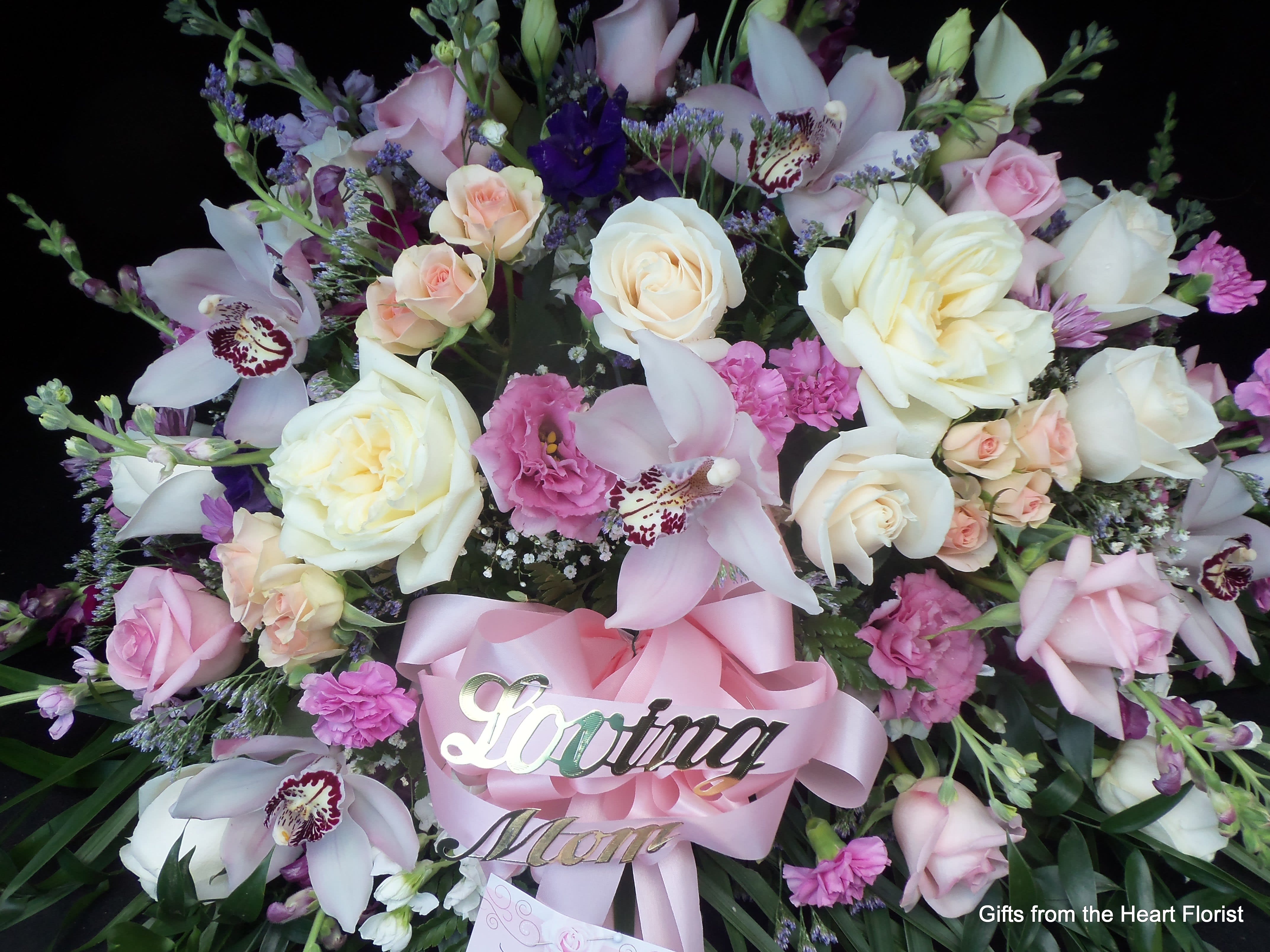 Pink and white floral spray with roses and orchids, accented by a pink ribbon