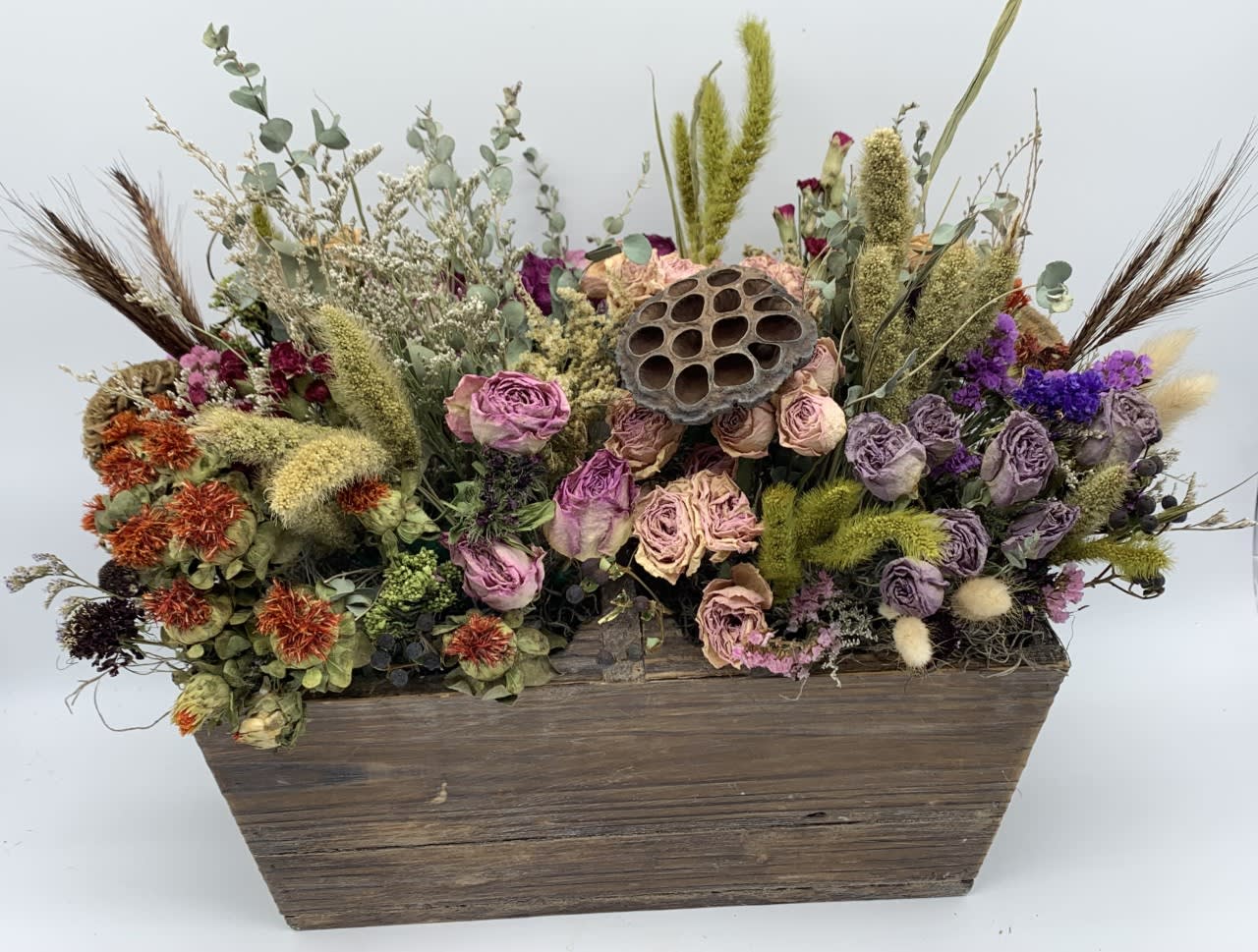 Dried flower arrangement in a wooden box with purple and peach blooms