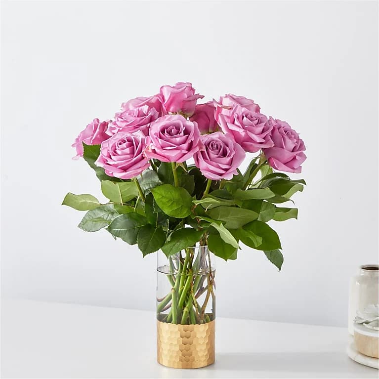 Pink roses arranged in a clear glass vase with a gold base