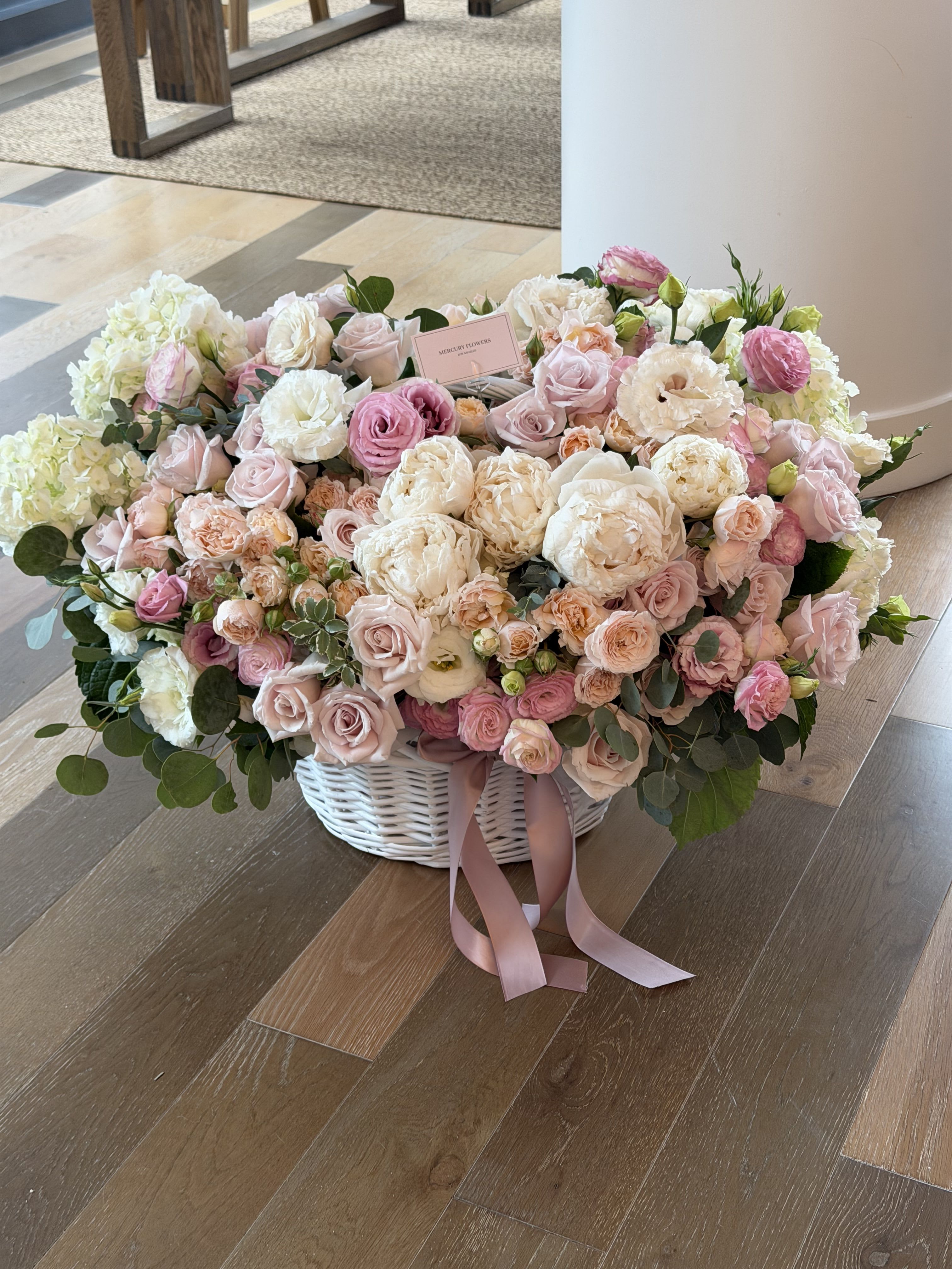 Large pastel flower arrangement in a white basket with pink ribbon