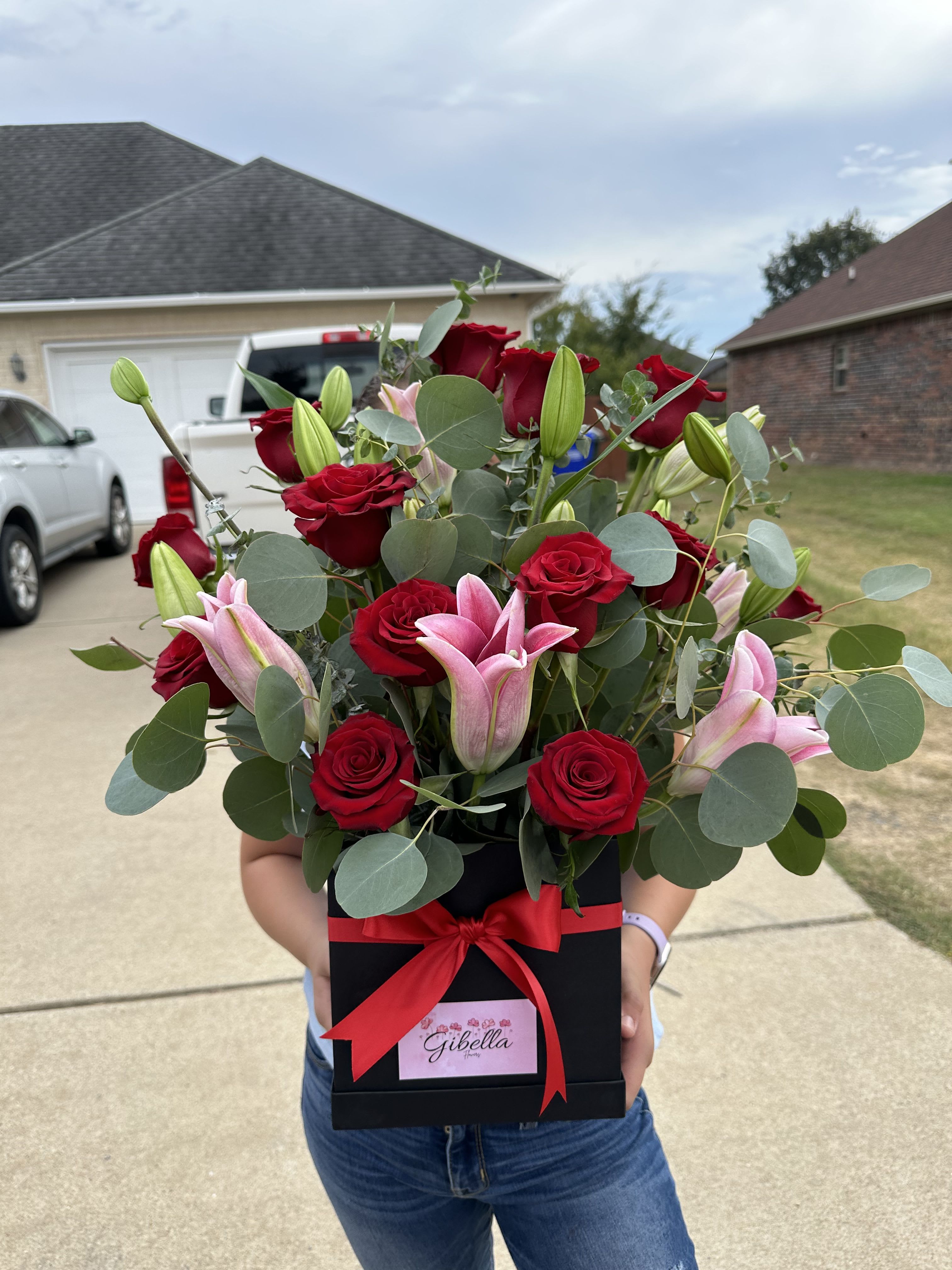 Bouquet of red roses and pink lilies in a black gift box with a red ribbon