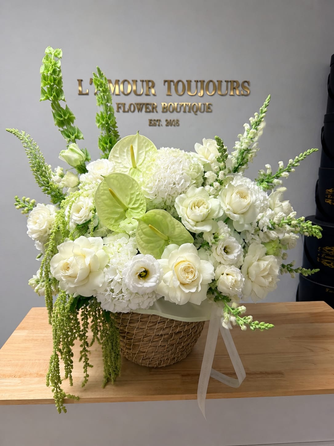 White floral arrangement in a wicker basket with green accents
