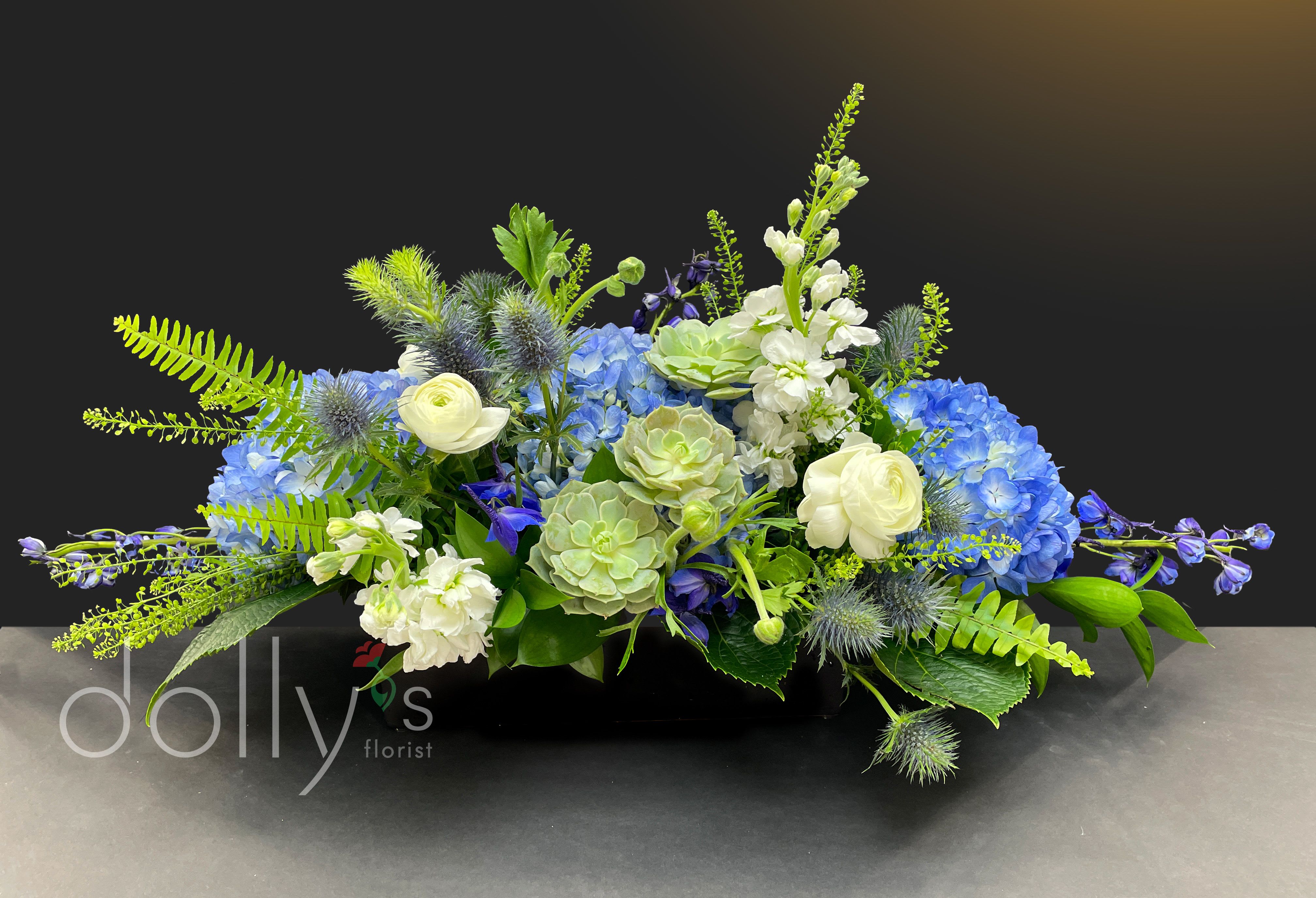 Low floral arrangement with blue hydrangeas, white blooms, and green succulents