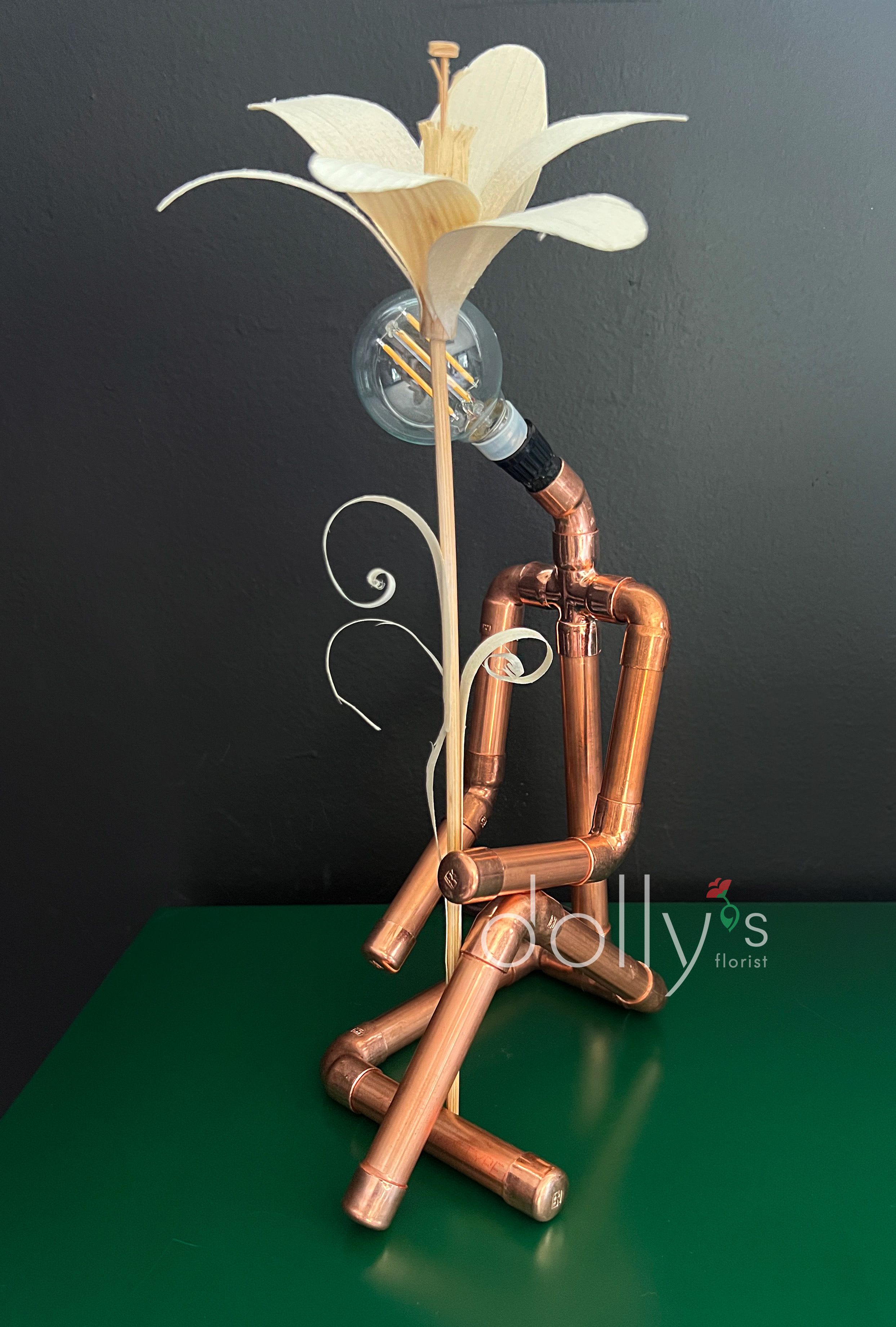 Copper pipe figure holding a white flower with a light bulb head