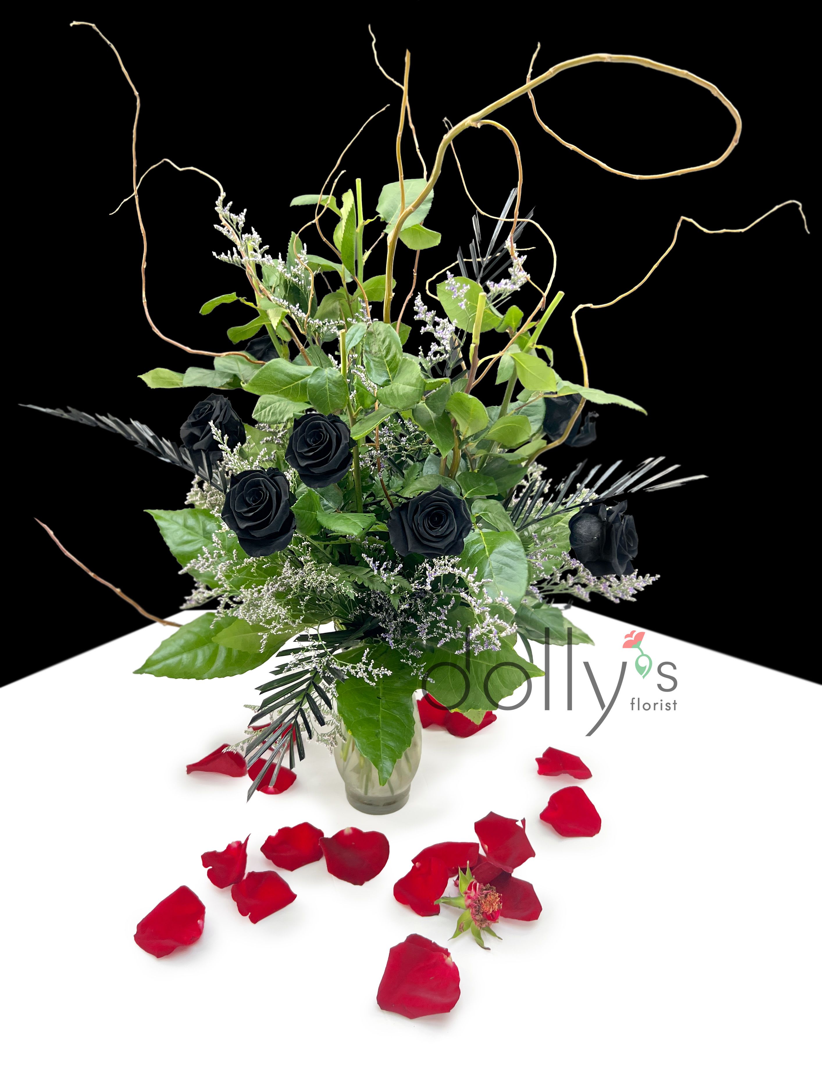Black roses in a glass vase with red rose petals around it