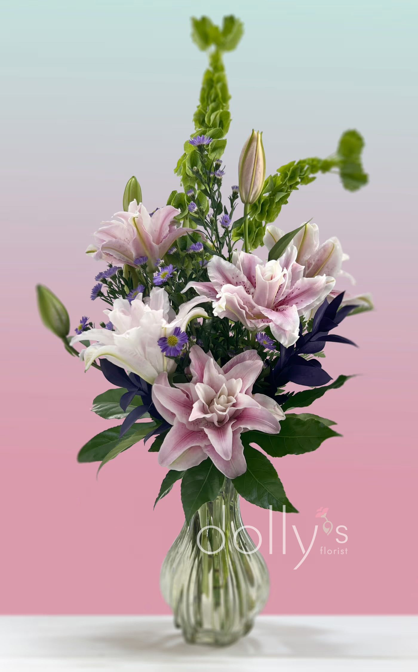 Pink and white lilies in a clear glass vase with purple accents