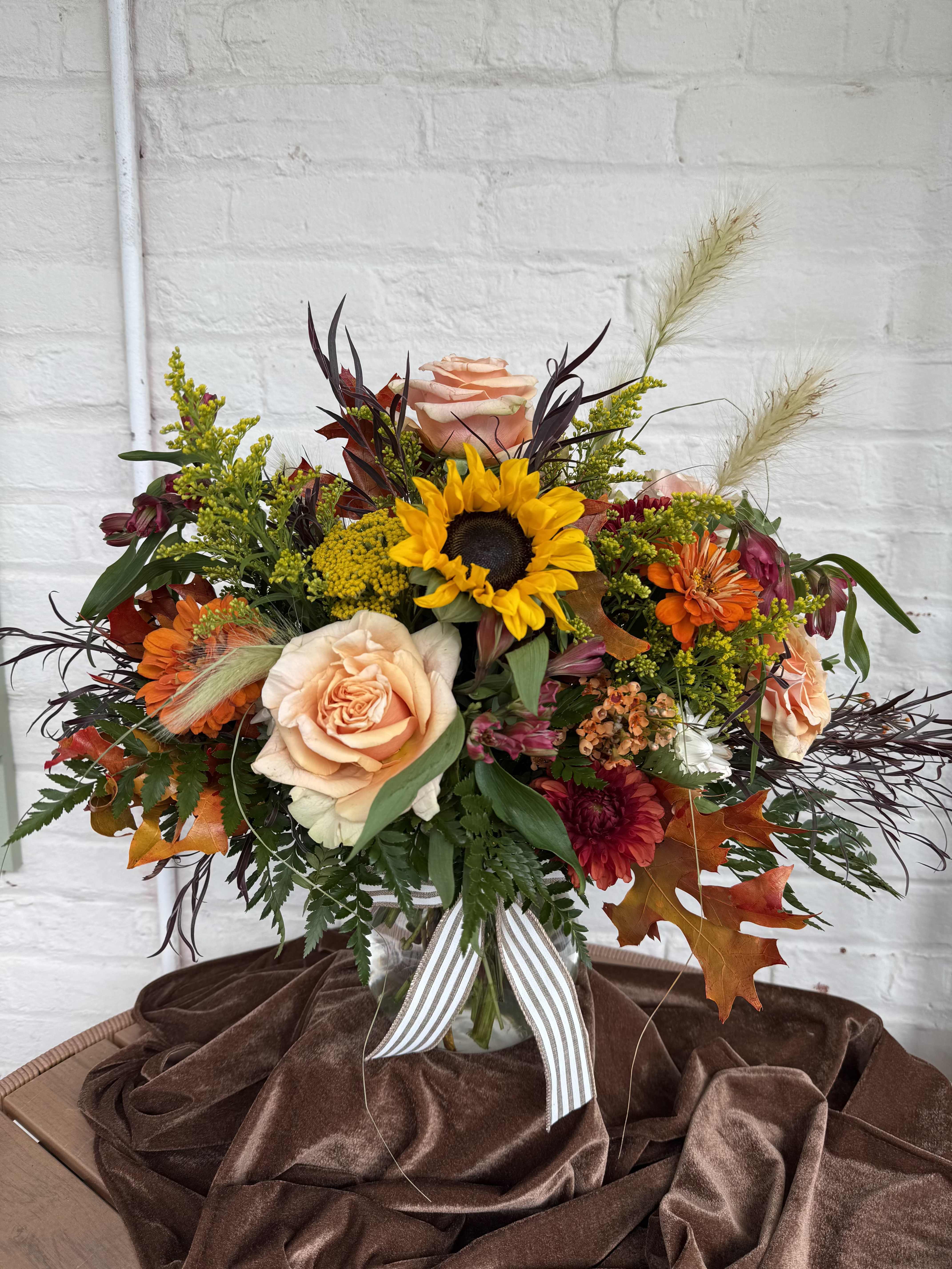 Mixed bouquet with a sunflower, peach roses, and orange blooms in a vase