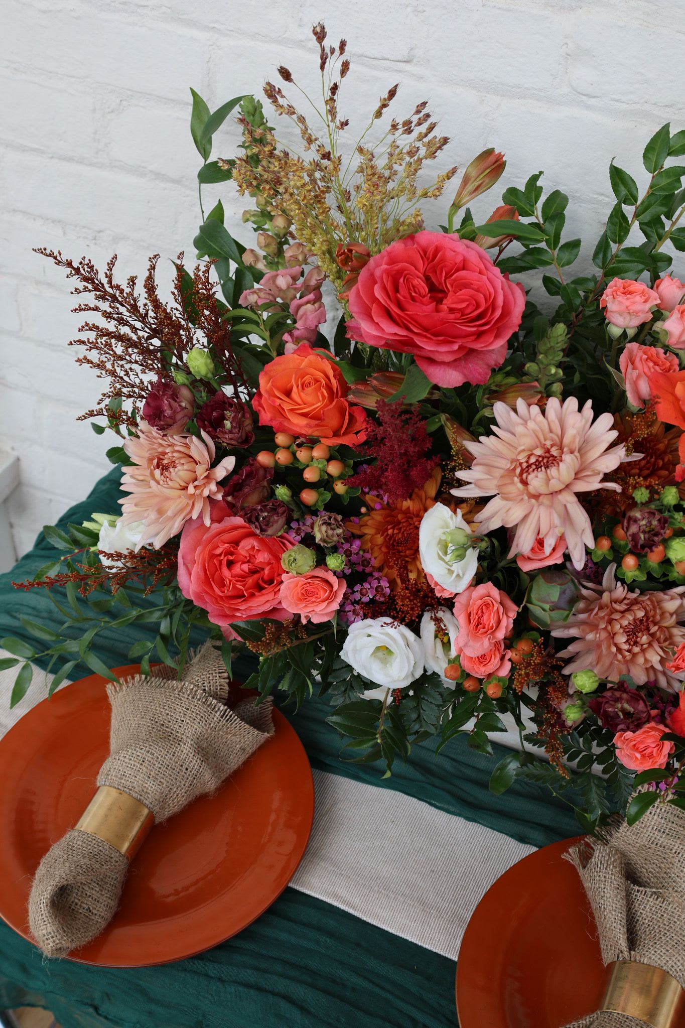 Colorful bouquet with roses, daisies, and mixed blooms beside orange plates