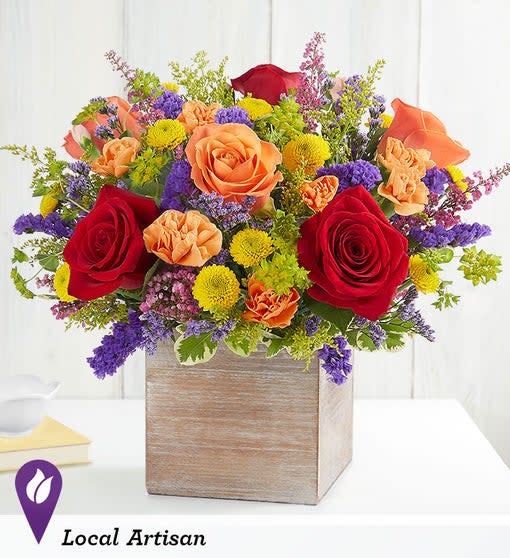 Mixed bouquet of red, orange, yellow, and purple flowers in a wooden box