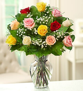 Mixed-color rose bouquet with white filler flowers arranged in a clear glass vase
