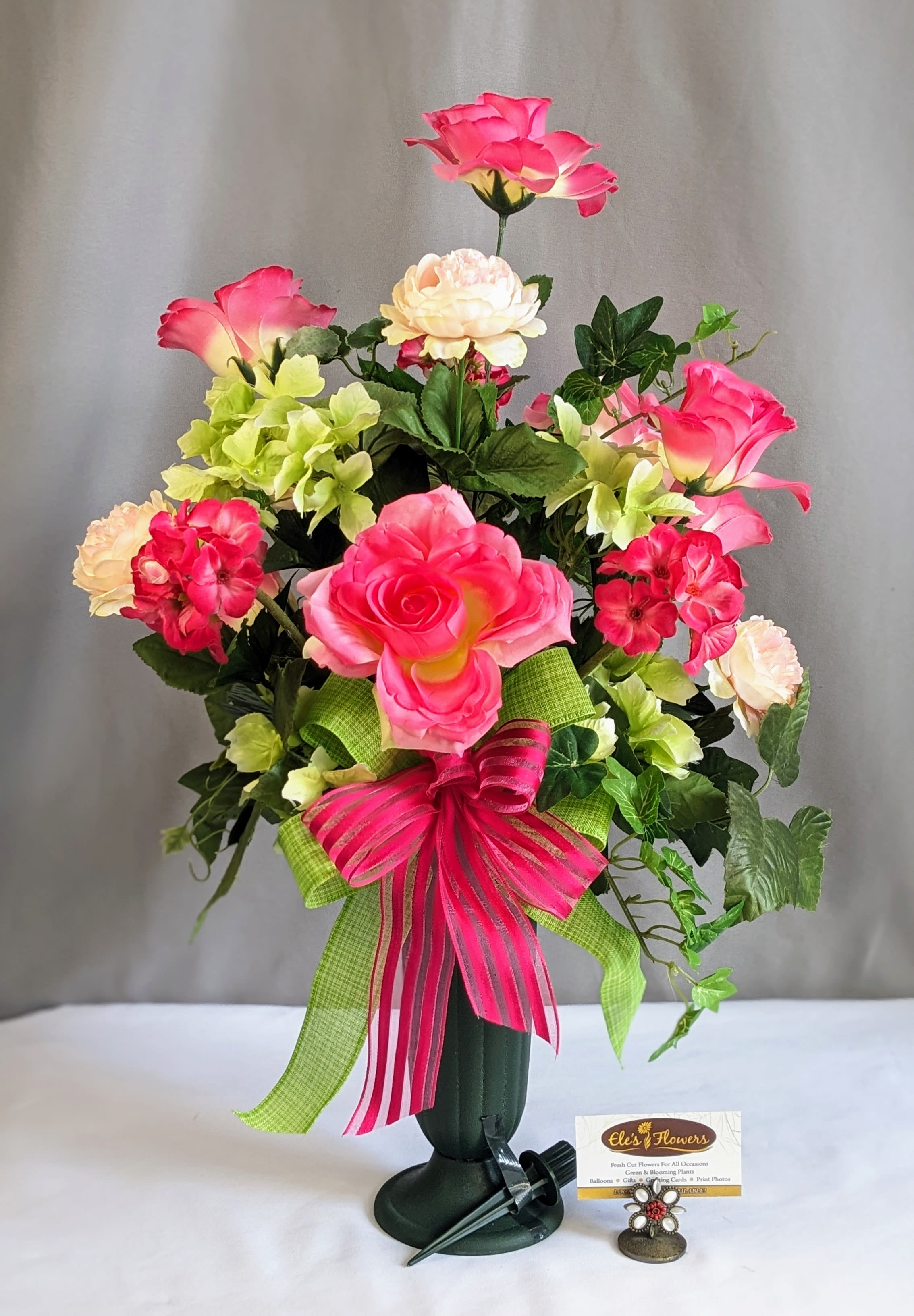 Memorial Graveside Cone Pinks/Greens - Artificial Arrangement - Honor and remember a cherished loved one with this beautifully designed memorial silk arrangement, thoughtfully created for placement beside a gravestone or memorial site. Arranged in a durable cone vase with an attached ground stake, this tribute can be securely placed into the ground near any headstone, making it a meaningful and lasting display for Memorial Day or everyday remembrance. Featuring a vibrant blend of pinks and greens it is accented with elegant ribbon and lush greenery, this arrangement offers a striking expression of love, honor, and remembrance. Crafted with high-end artificial flowers, it is weatherproof and designed to maintain its beauty through the outdoor elements season after season.  We would be happy to deliver this to your loved one's gravestone, please provide information on location in the special instructions or give us a call at 715.644.3537  Approximate Dimensions: 26"H x 17"W
