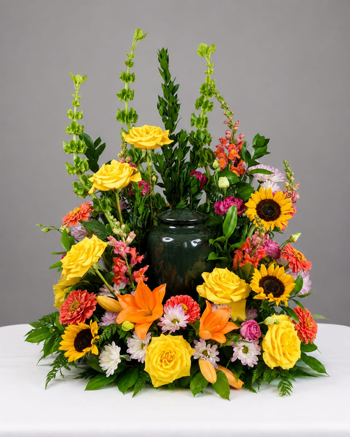 Colorful floral arrangement with yellow roses, sunflowers, and orange lilies in a dark vase