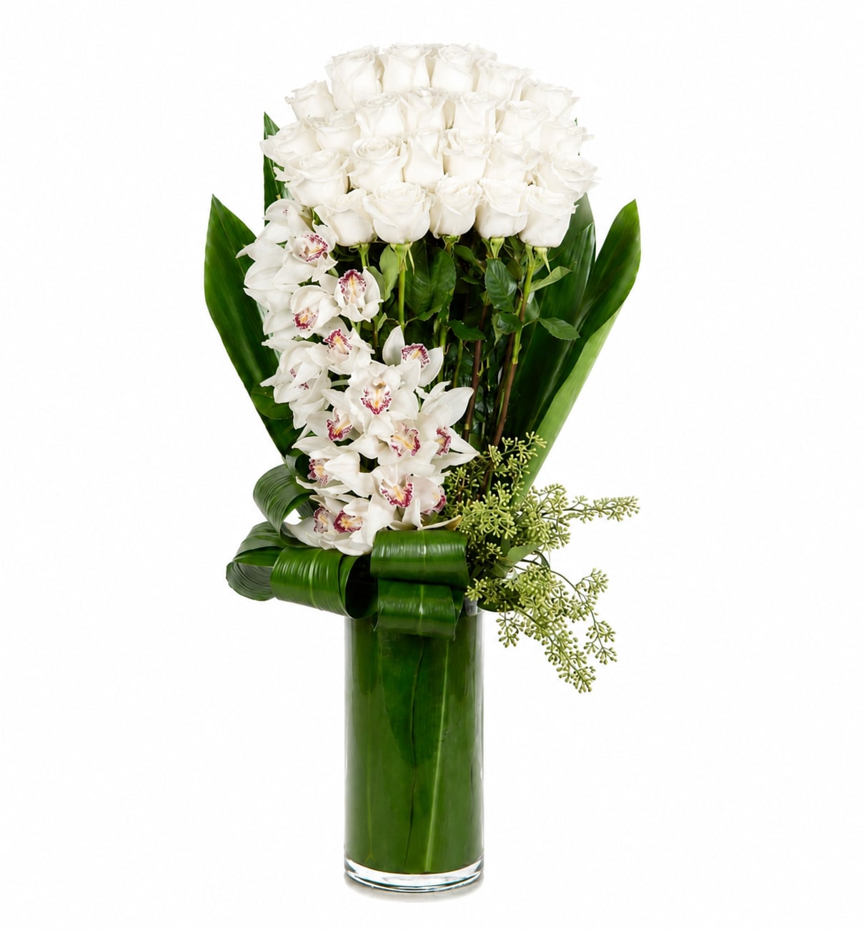 White roses and orchids in a tall glass vase with broad green leaves