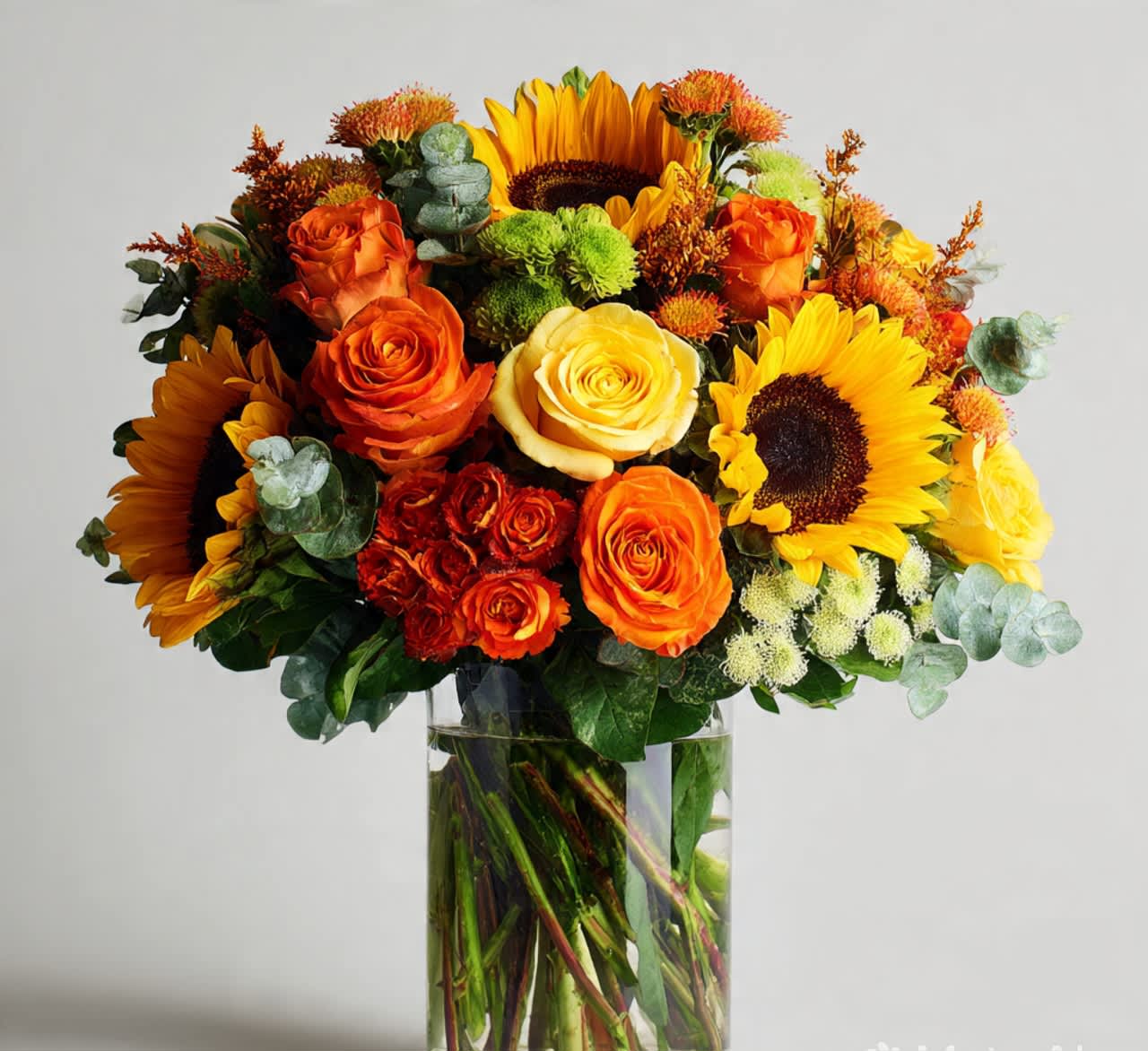 Bouquet of sunflowers and orange roses in a clear glass vase