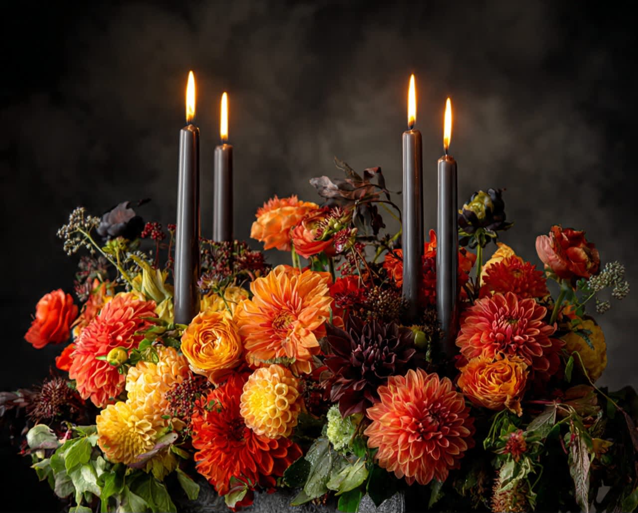 Orange and yellow floral arrangement with lit black taper candles