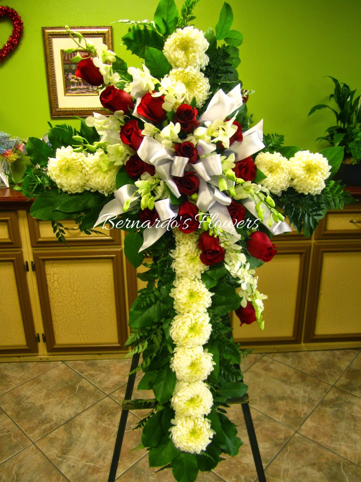 Cross-shaped floral tribute with red roses and white flowers on an easel