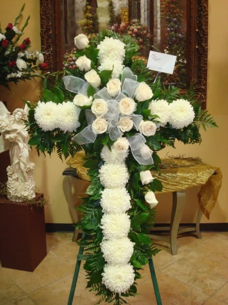 White floral cross arrangement with roses and ribbon on an easel