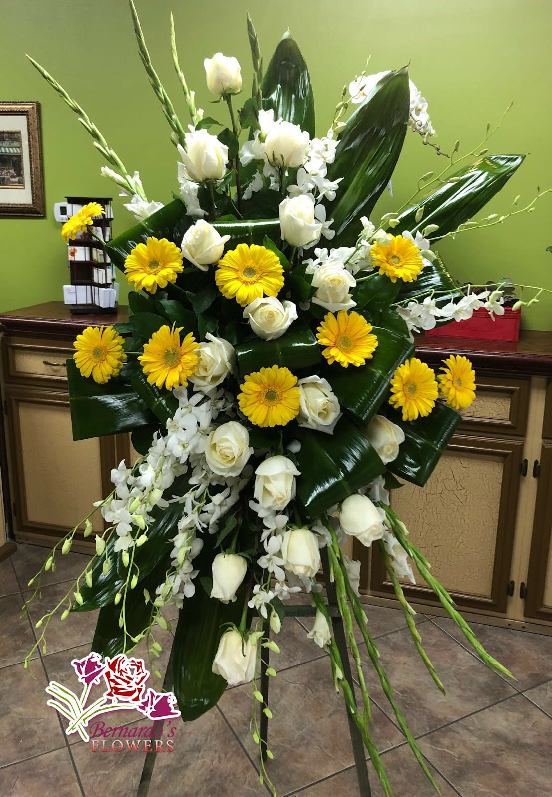 Tall floral standing spray with white roses, yellow gerbera daisies, and orchids
