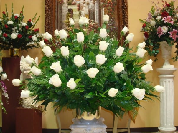 Large white rose arrangement in a gold vase with greenery
