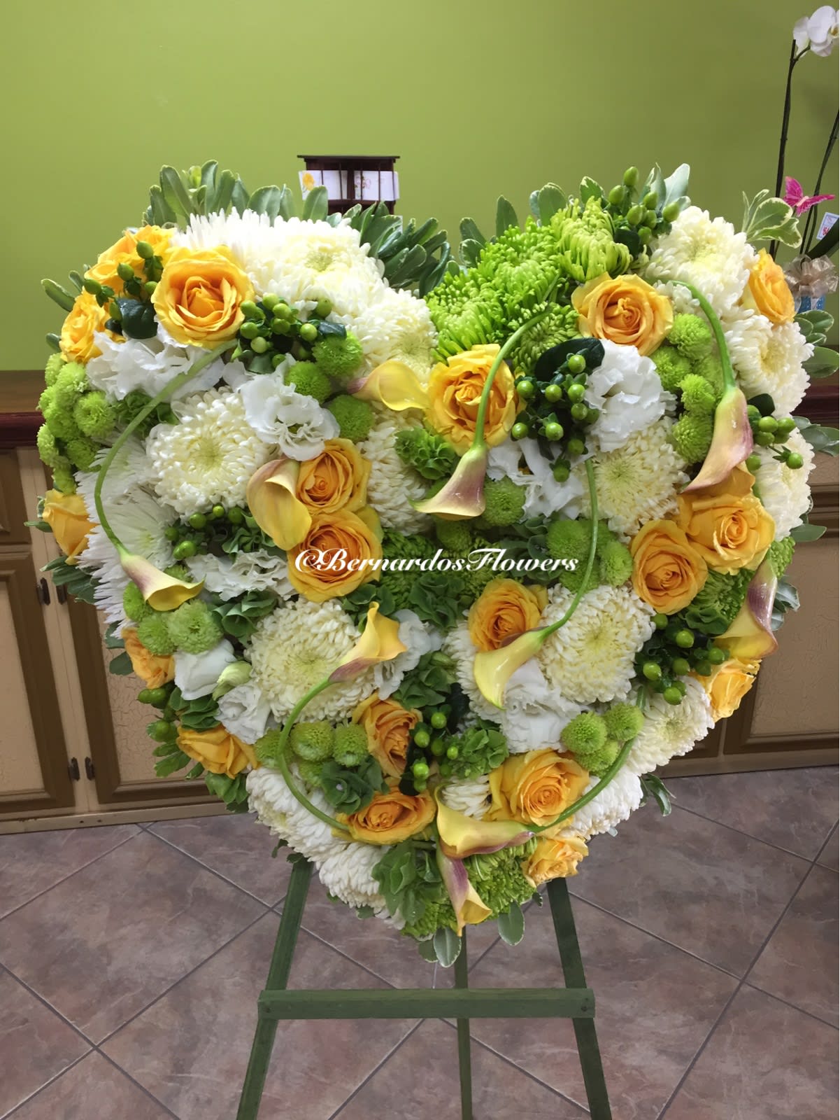 Heart-shaped floral arrangement with yellow roses, white blooms, and calla lilies on an easel