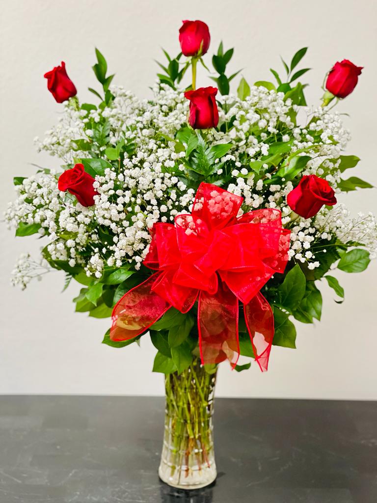 Red roses and white baby's breath in a clear glass vase with a red bow