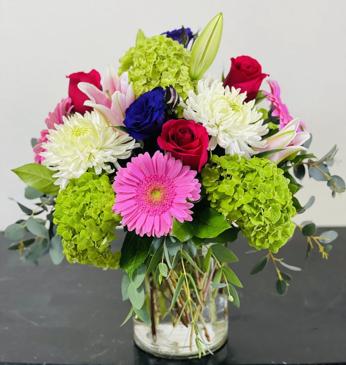 Mixed bouquet with roses, gerbera daisies, chrysanthemums, and hydrangeas in a glass vase