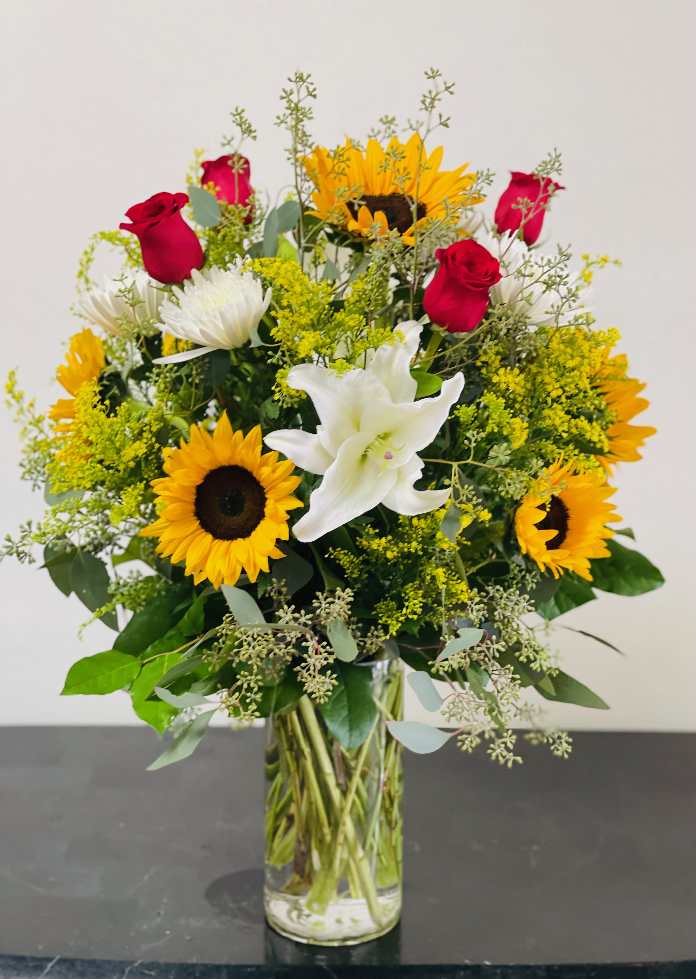 Bouquet of sunflowers, red roses, and white lilies in a glass vase