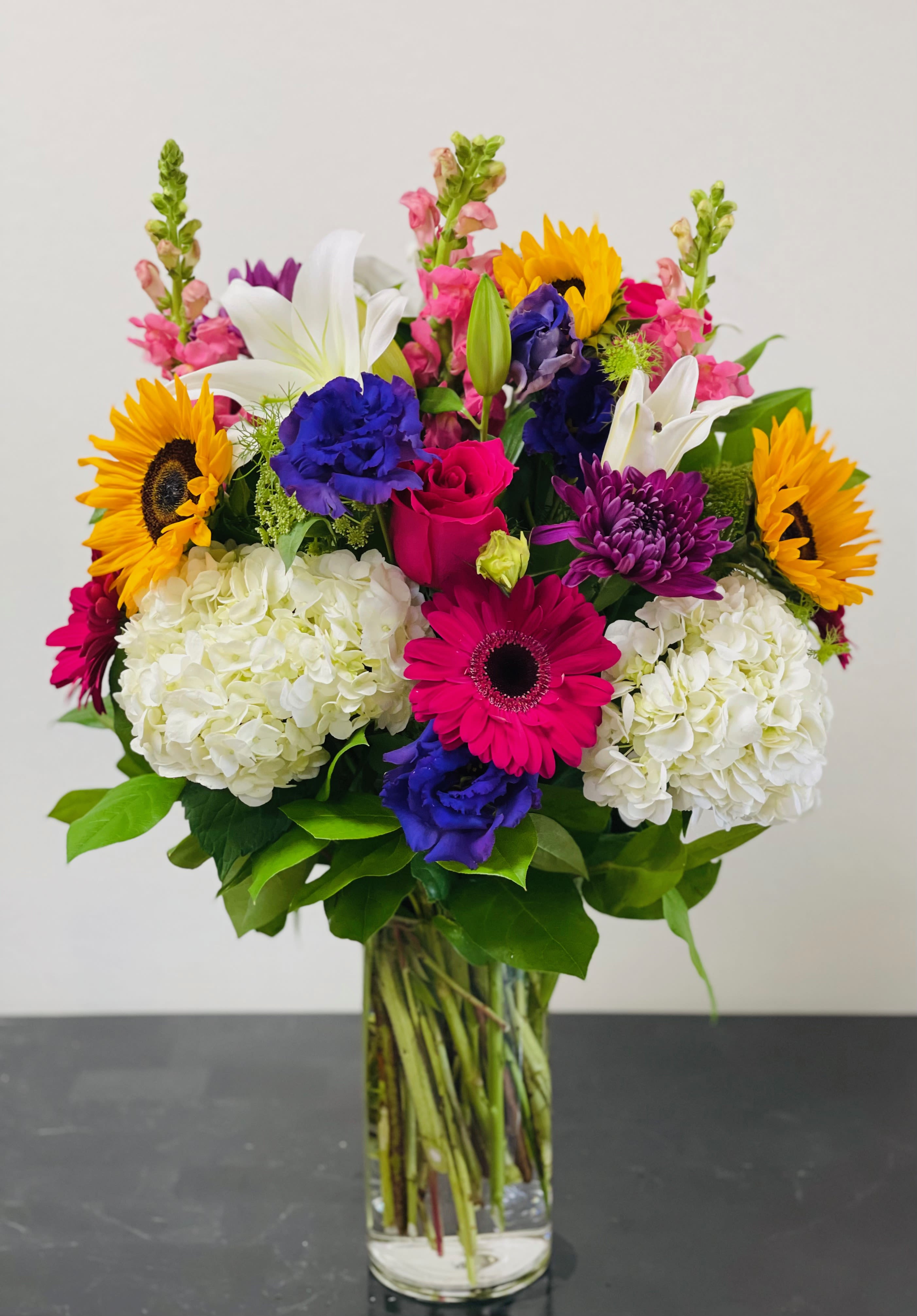 Colorful mixed bouquet in a clear glass vase with sunflowers, lilies, and hydrangeas