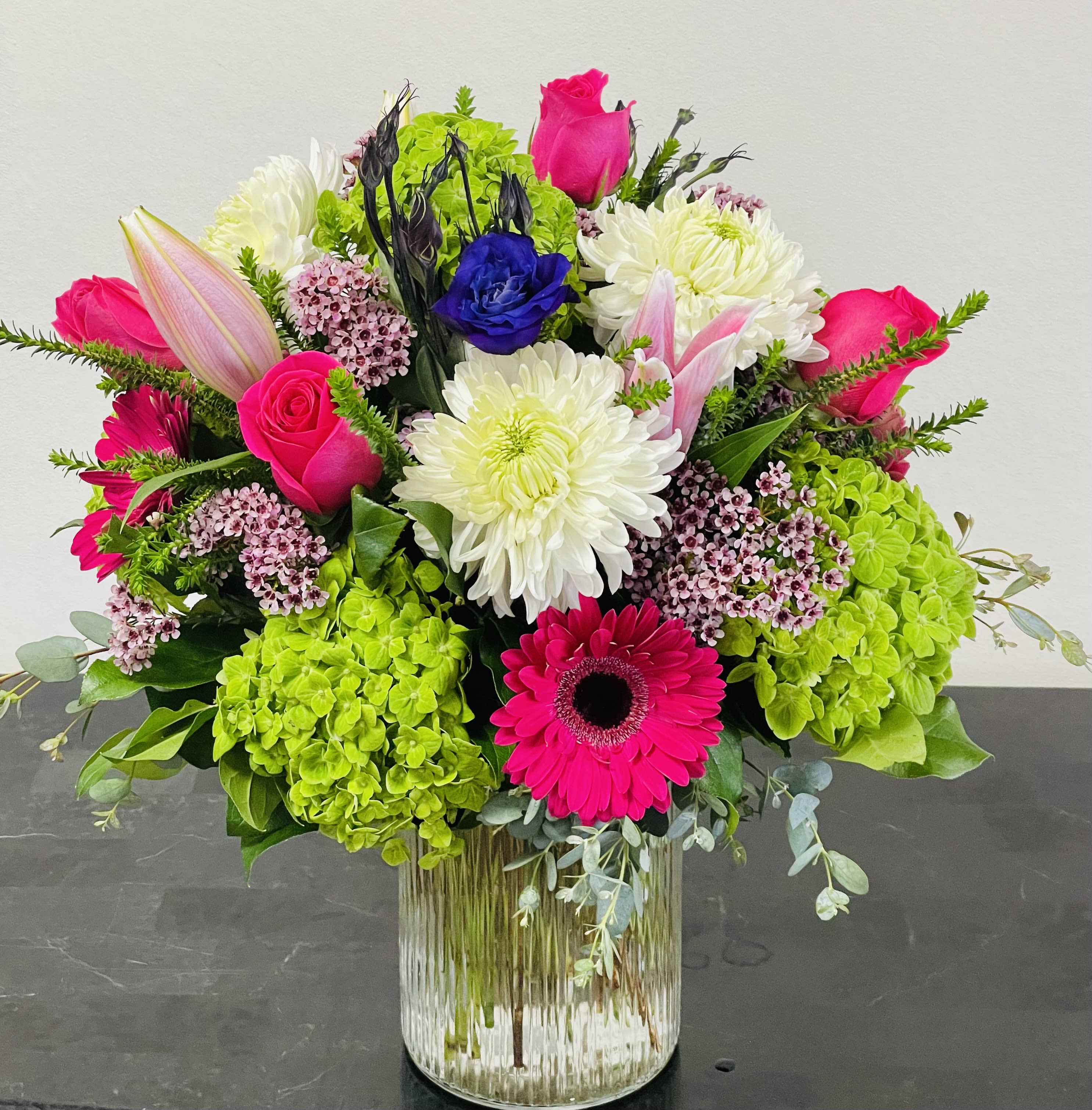 Bright mixed bouquet in a clear glass vase with pink, white, blue, and green blooms