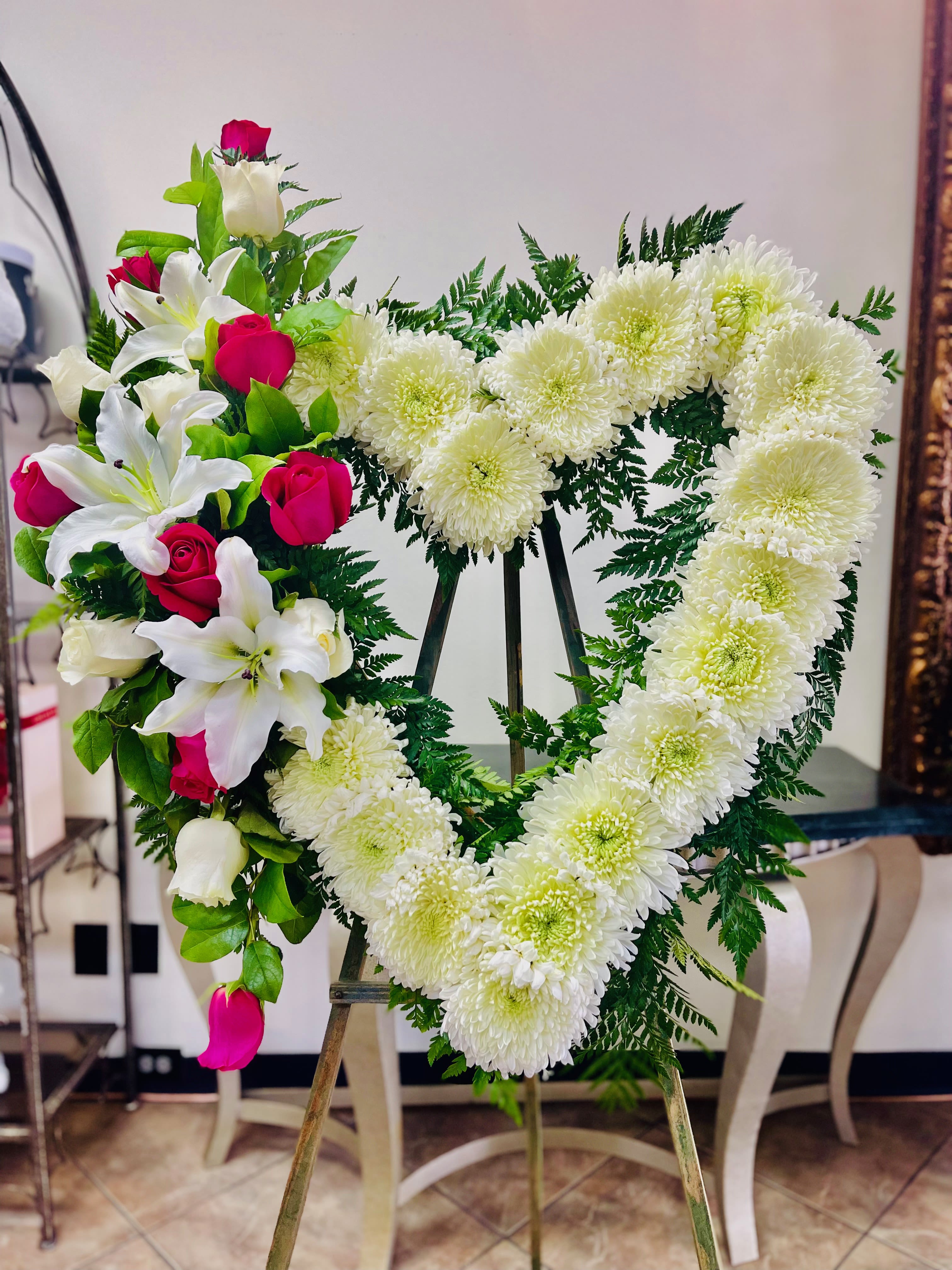 Heart-shaped floral wreath with white chrysanthemums and red roses on an easel