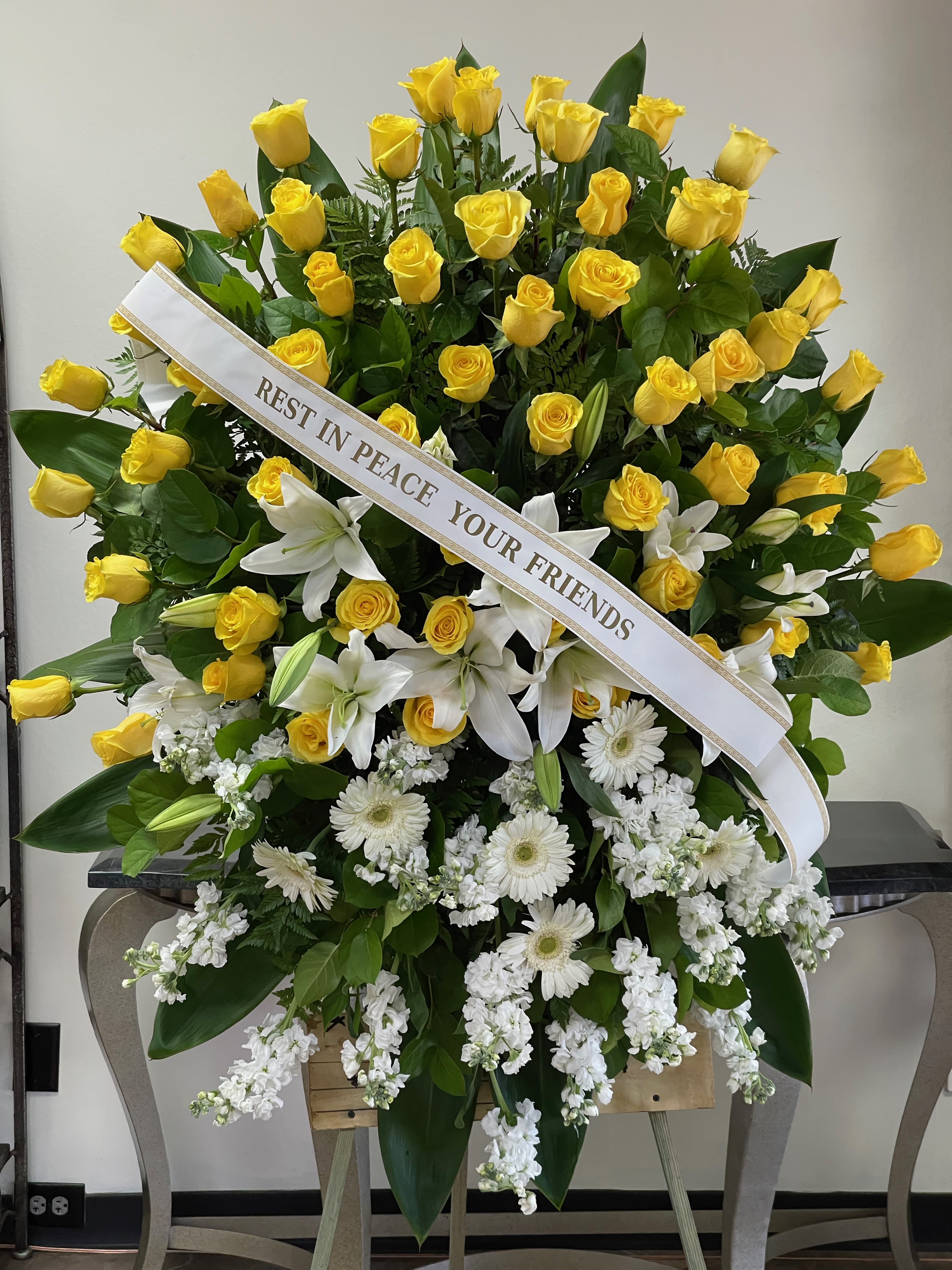 Large funeral spray of yellow roses and white lilies with a memorial ribbon
