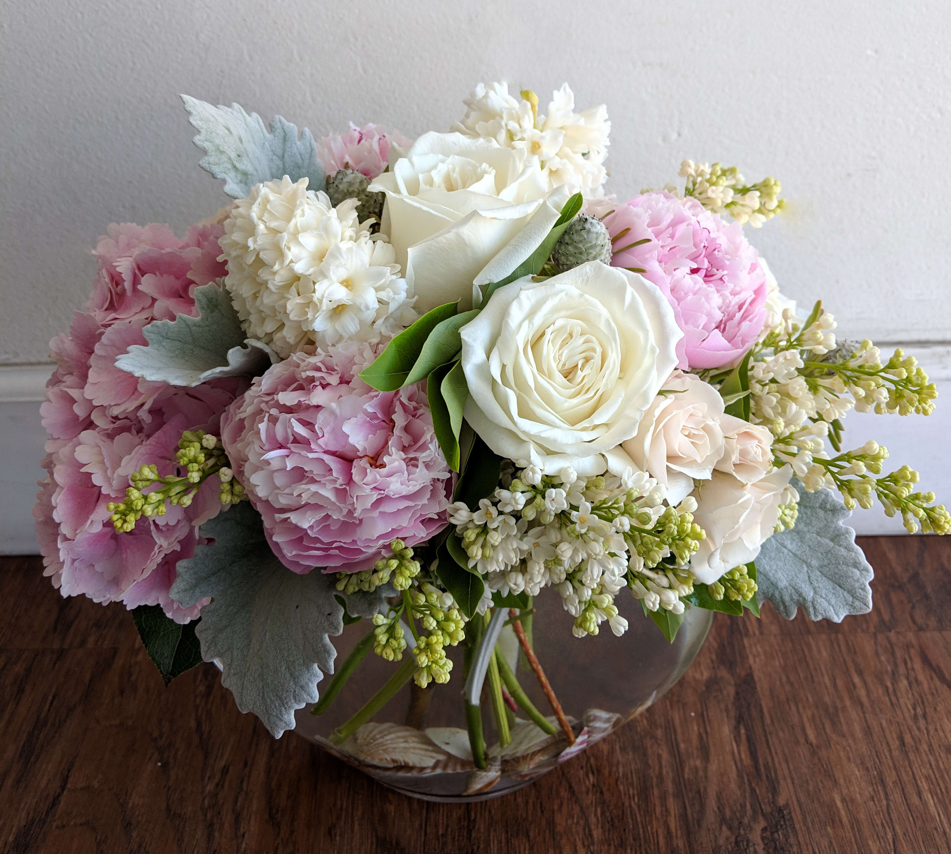 Pink and white bouquet of roses, peonies, and small white flowers in a glass vase